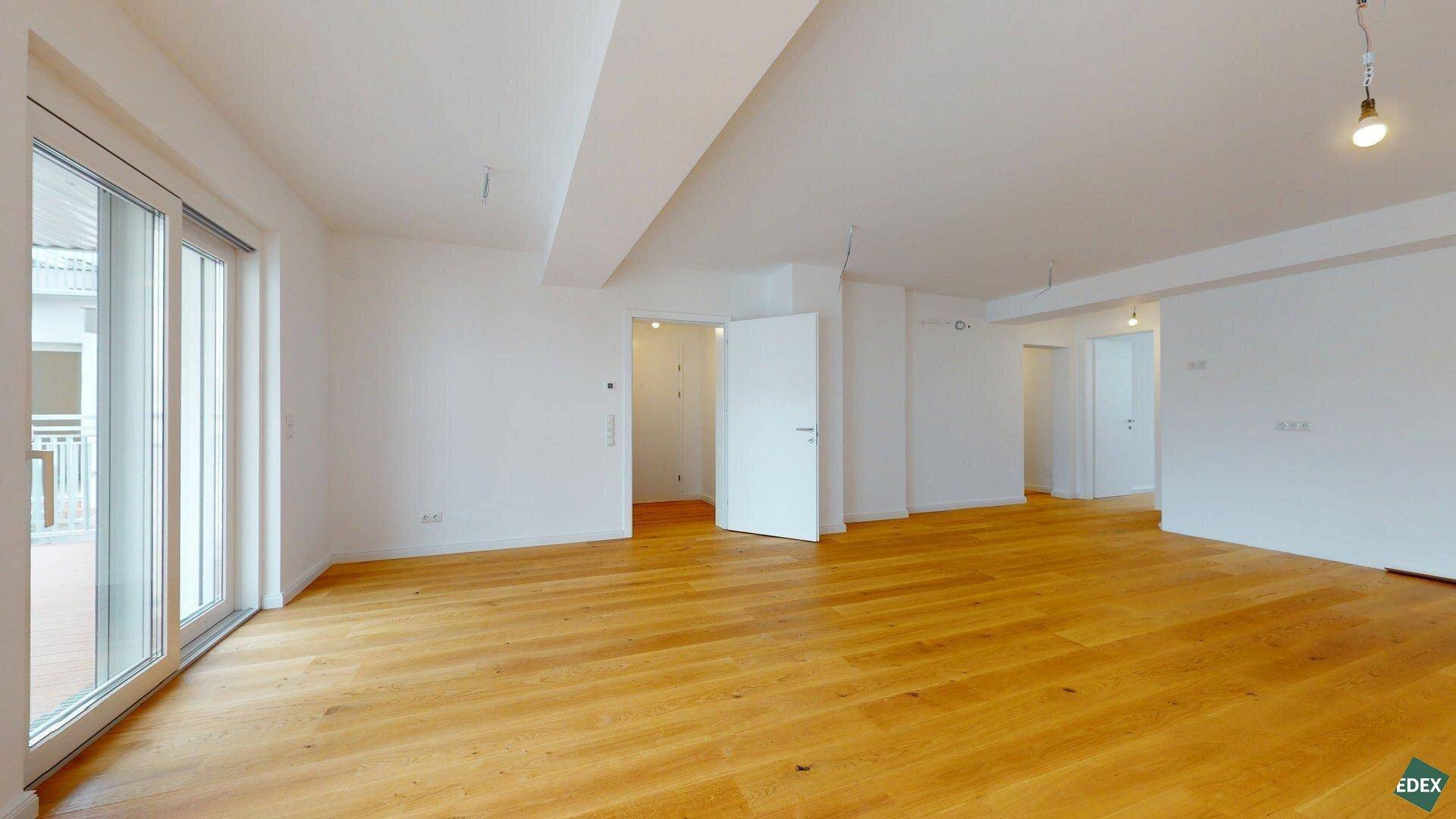 Geräumiger Wohnbereich mit Holzboden, weiß gestrichenen Wänden und Balkonzugang.