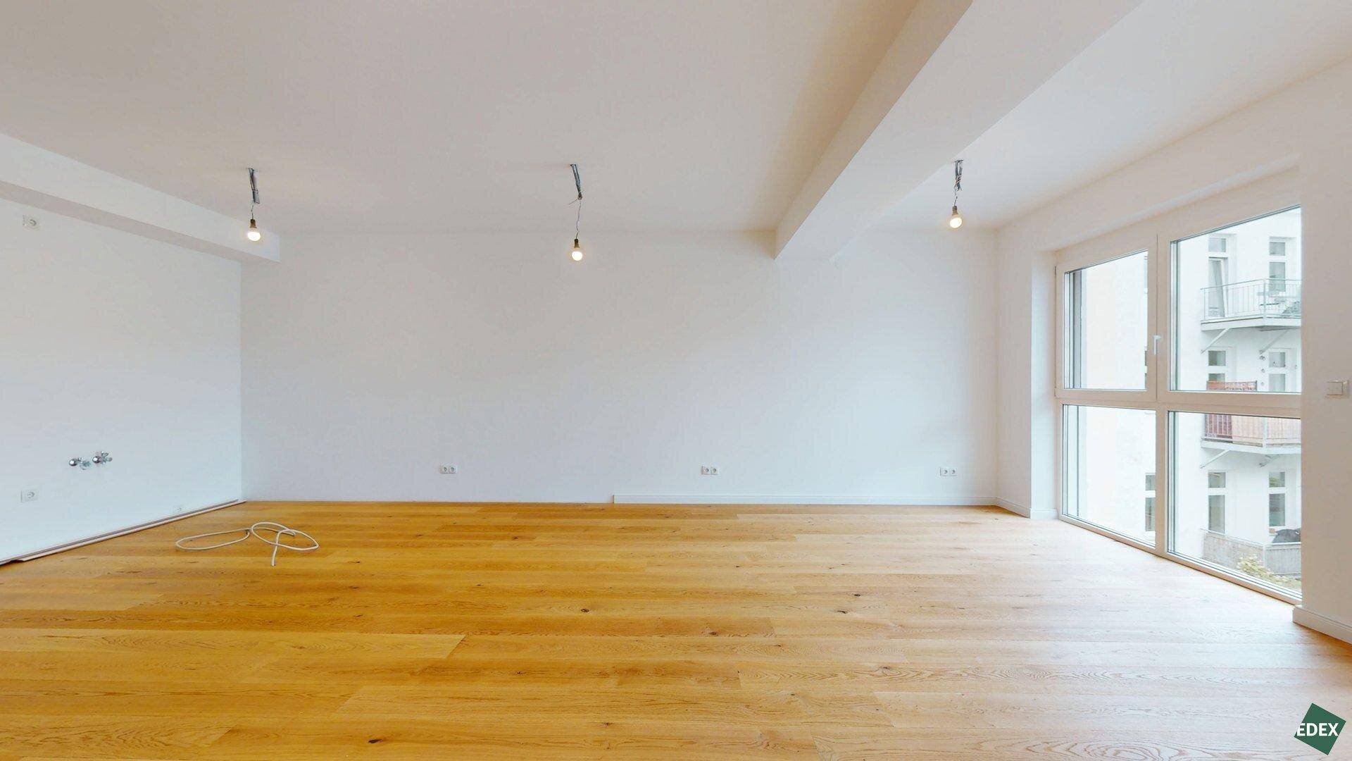 Lichtdurchfluteter Wohnbereich mit hellem Holzfußboden und großen Fenstern zur Straßenseite.