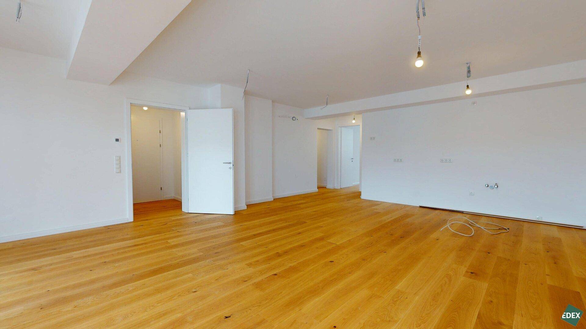 Großer, leerer Wohnraum mit hellem Parkettboden und mehreren Türen zu angrenzenden Zimmern.