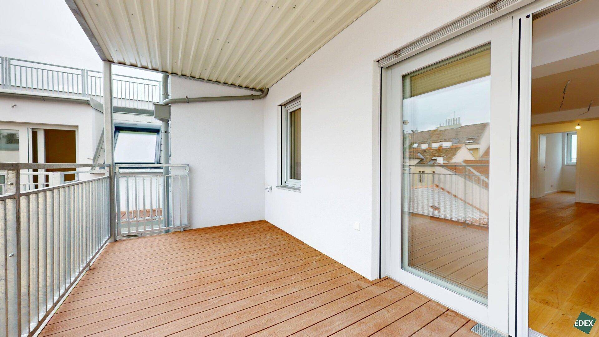 Geräumiger Balkon mit Holzboden und Metallgeländer, ideal für entspannte Stunden im Freien.