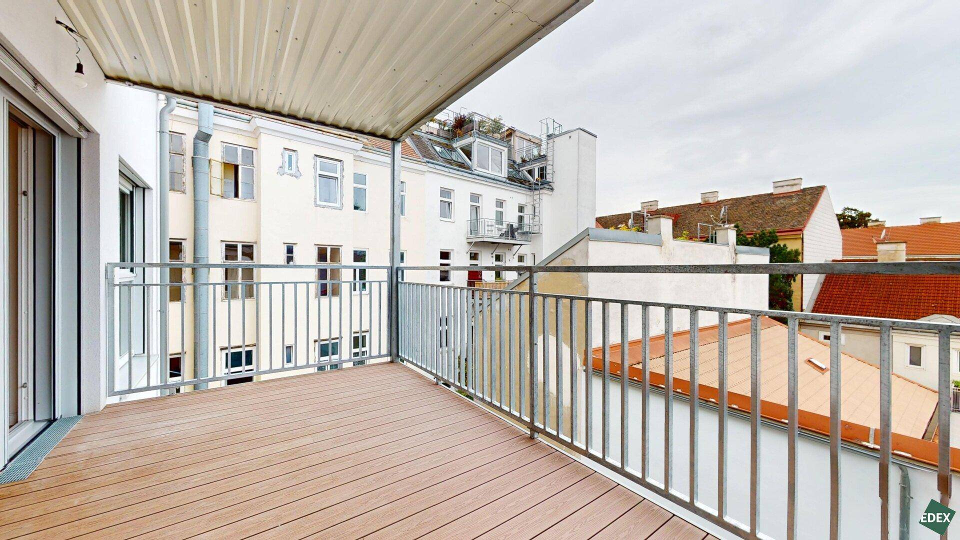 Balkon mit Holzboden und Blick auf die umliegenden Gebäude und Dächer der Stadt.