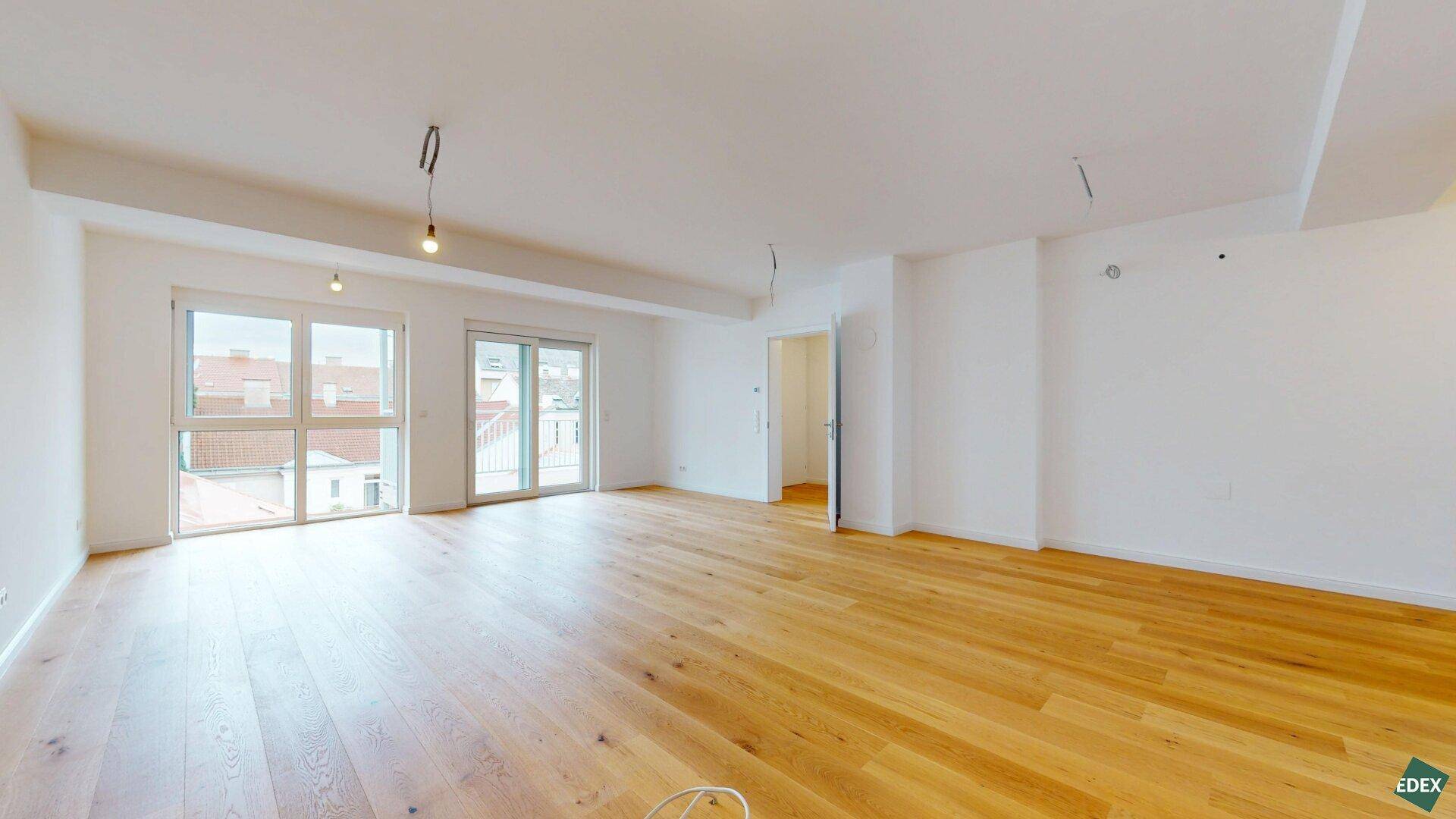 Geräumiger, heller Wohnbereich mit neuem Holzparkettboden und Zugang zu einem Balkon.