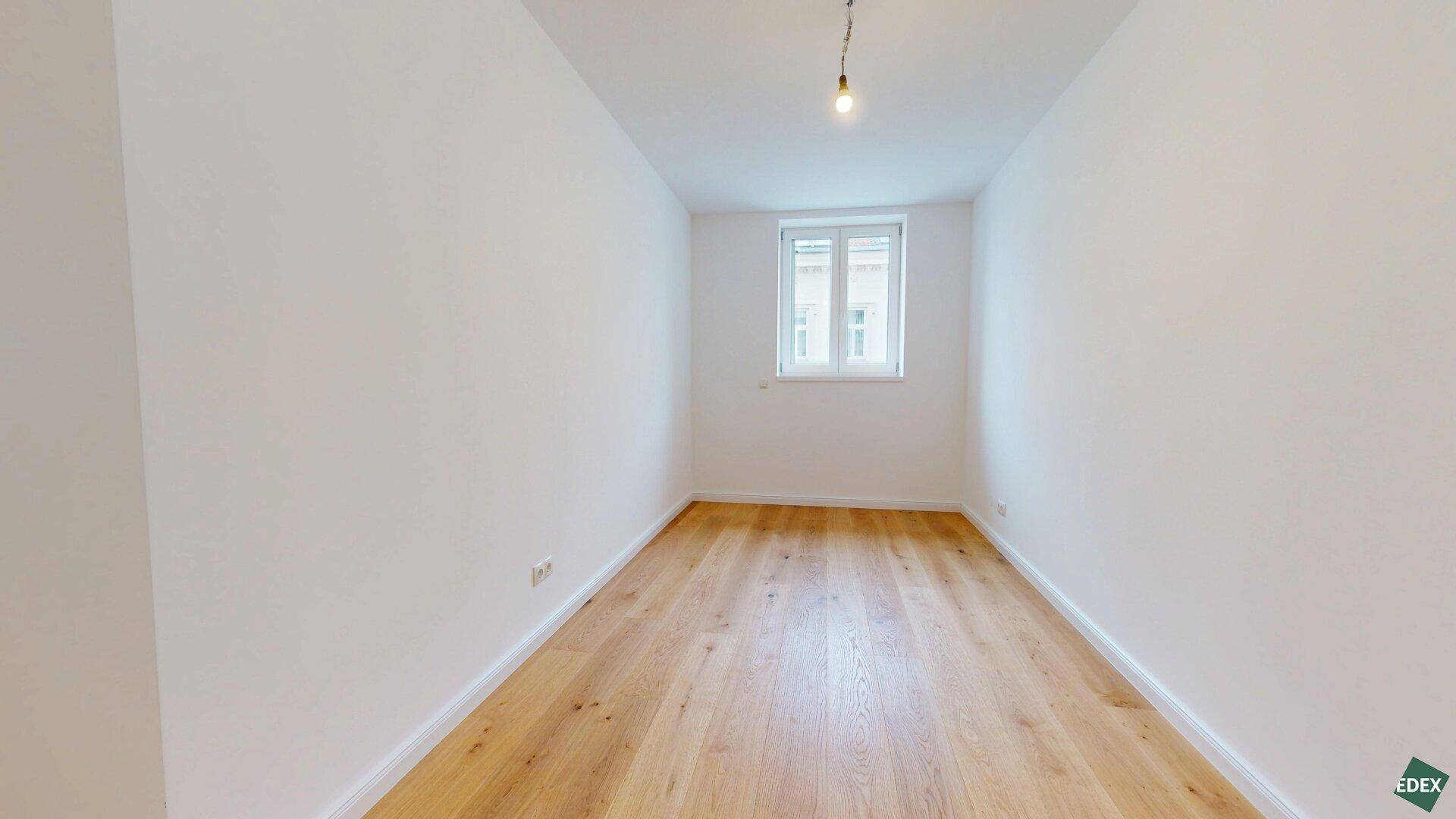 Helles, leeres Zimmer mit Holzparkettboden und einem Fenster, ideal als Schlaf- oder Arbeitszimmer.
