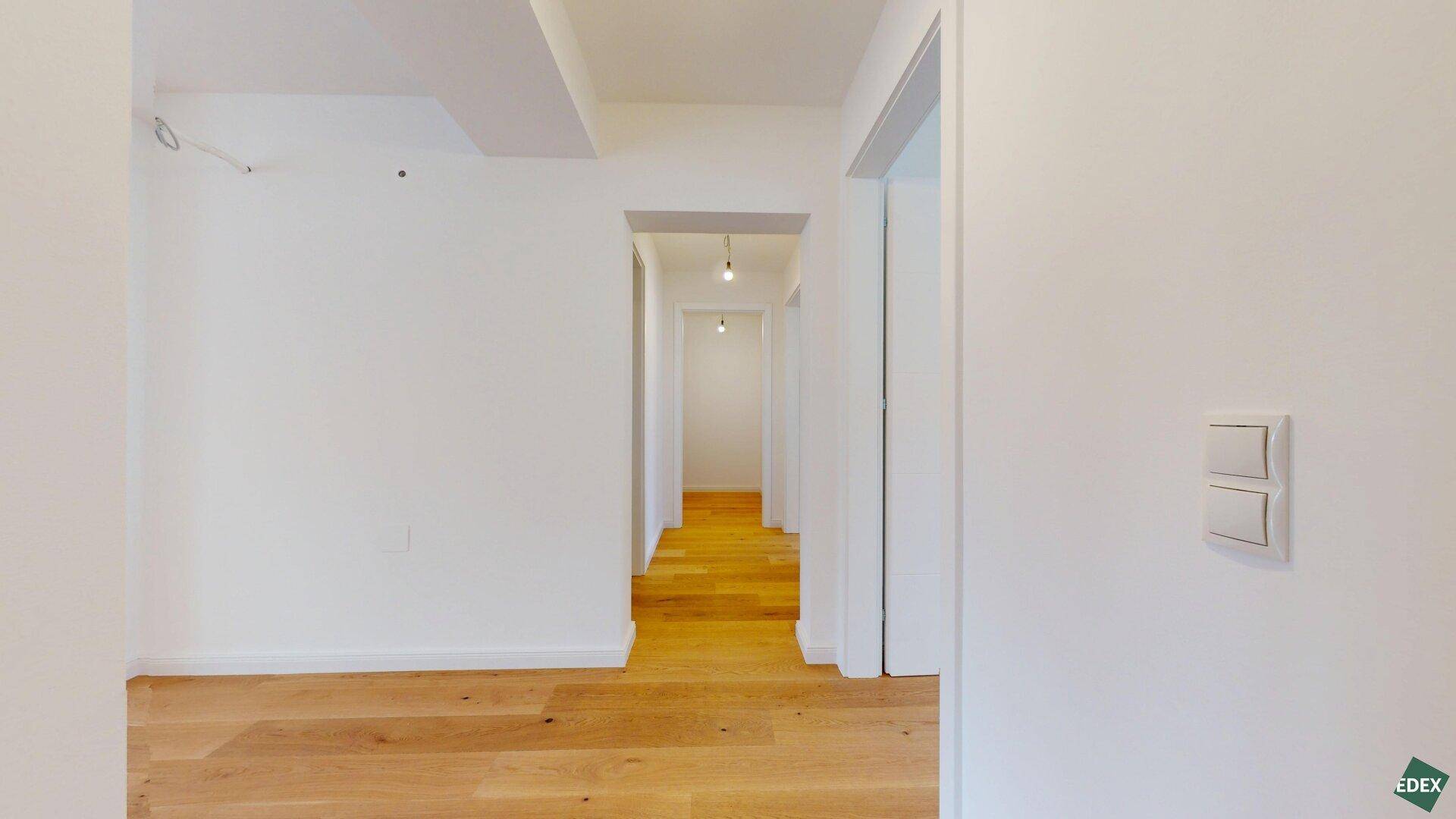 Langer, heller Flur mit Holzparkettboden, der zu den verschiedenen Räumen der Wohnung führt.