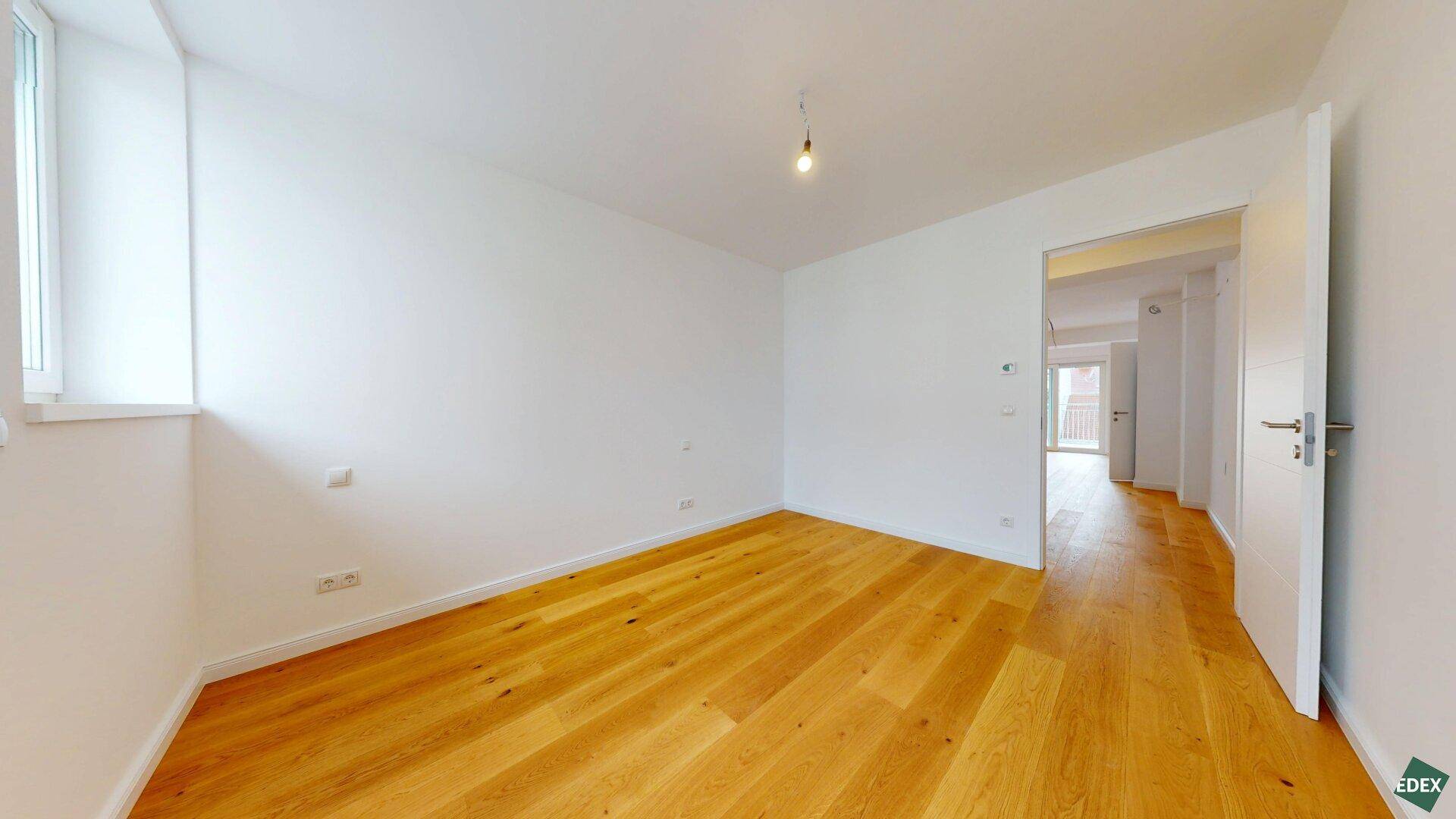 Geräumiges, helles Zimmer mit Holzparkettboden und einem Fenster, bereit zur individuellen Gestaltung.