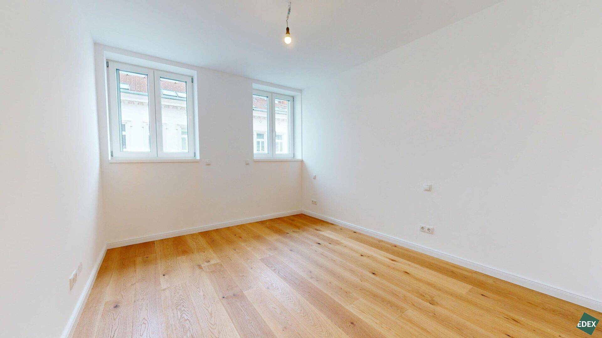 Helles Schlafzimmer mit zwei Fenstern und neuem Holzparkettboden, bietet viel Tageslicht.