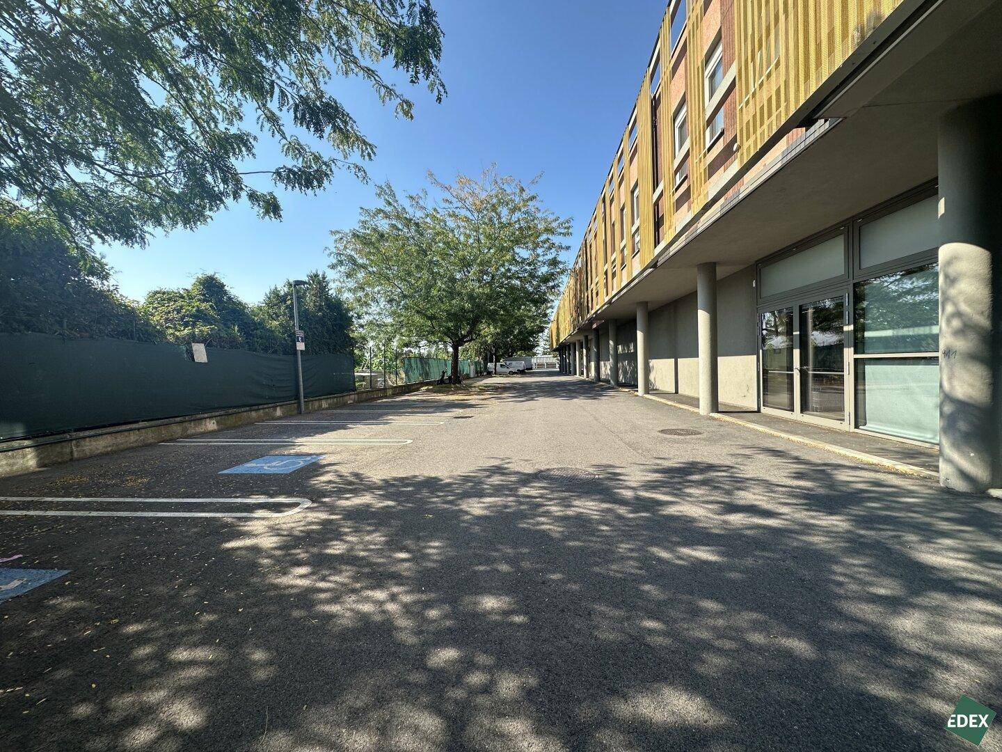 Außenansicht eines modernen Gebäudes mit angrenzendem Parkplatz und Bäumen unter blauem Himmel.