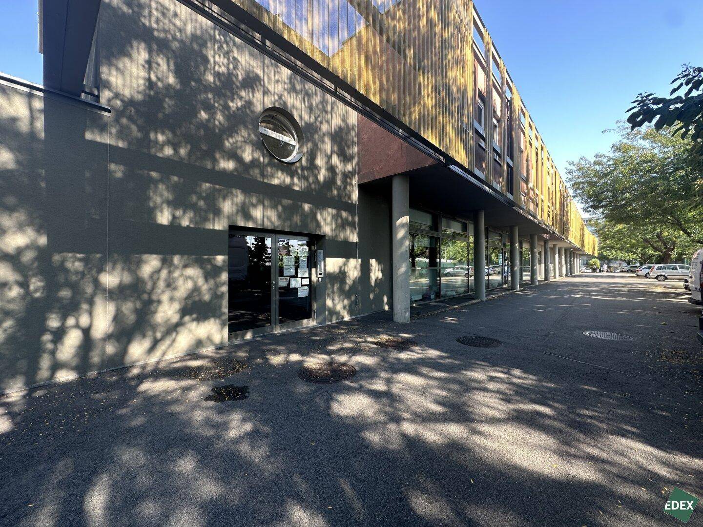 Moderne Gebäudefassade mit großen Fenstern und Parkplätzen an einem sonnigen Tag.