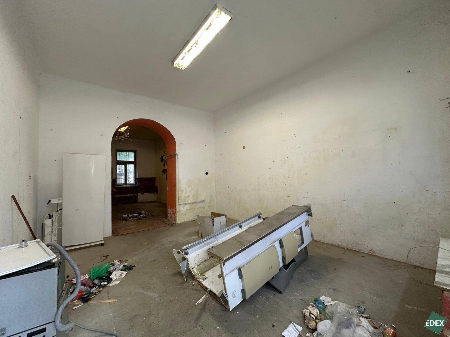 Unaufgeräumter Raum in Renovierung mit sichtbaren Gebrauchsspuren und einem Kühlschrank.