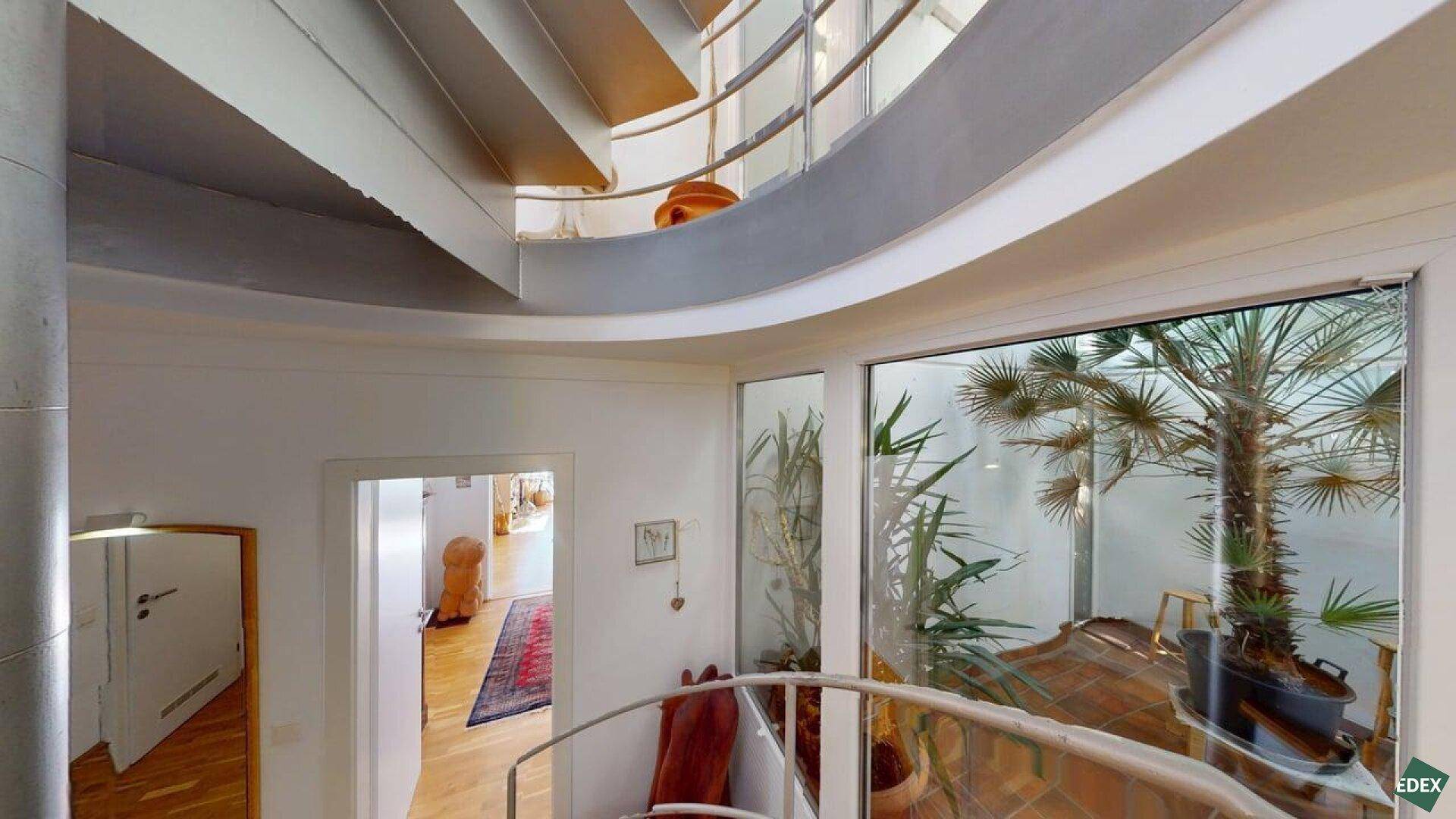 Heller Flur mit moderner Wendeltreppe und Blick in einen verglasten Innenhof mit Pflanzen.