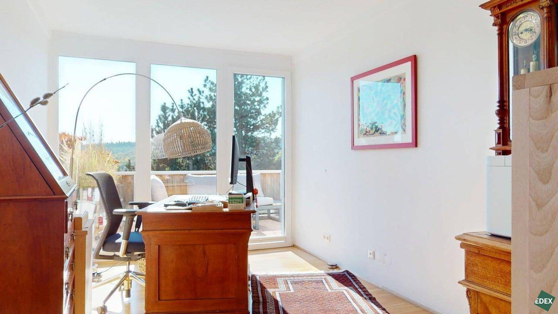Helles Arbeitszimmer mit Holztisch, Bürostuhl und Zugang zu einem Balkon oder einer Terrasse.