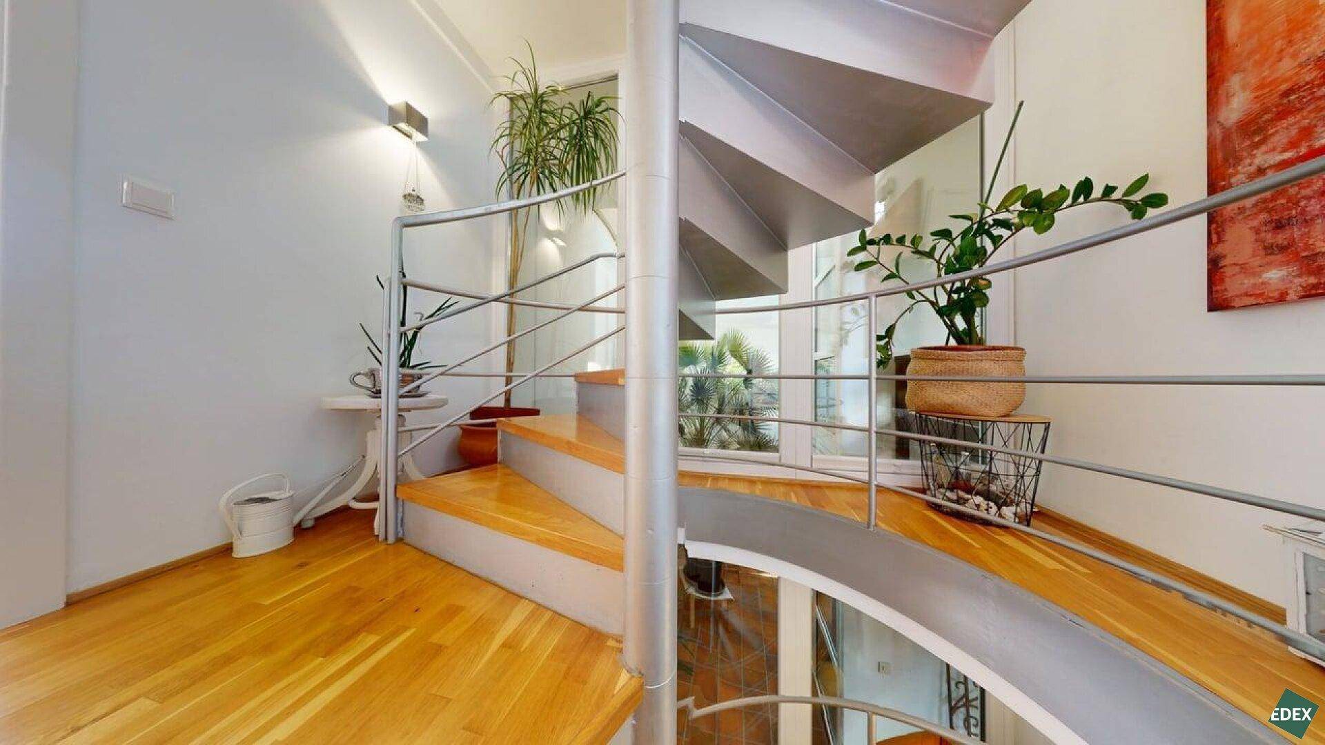 Elegante Wendeltreppe mit Holzstufen und Metallgeländer in einem hellen Eingangsbereich.