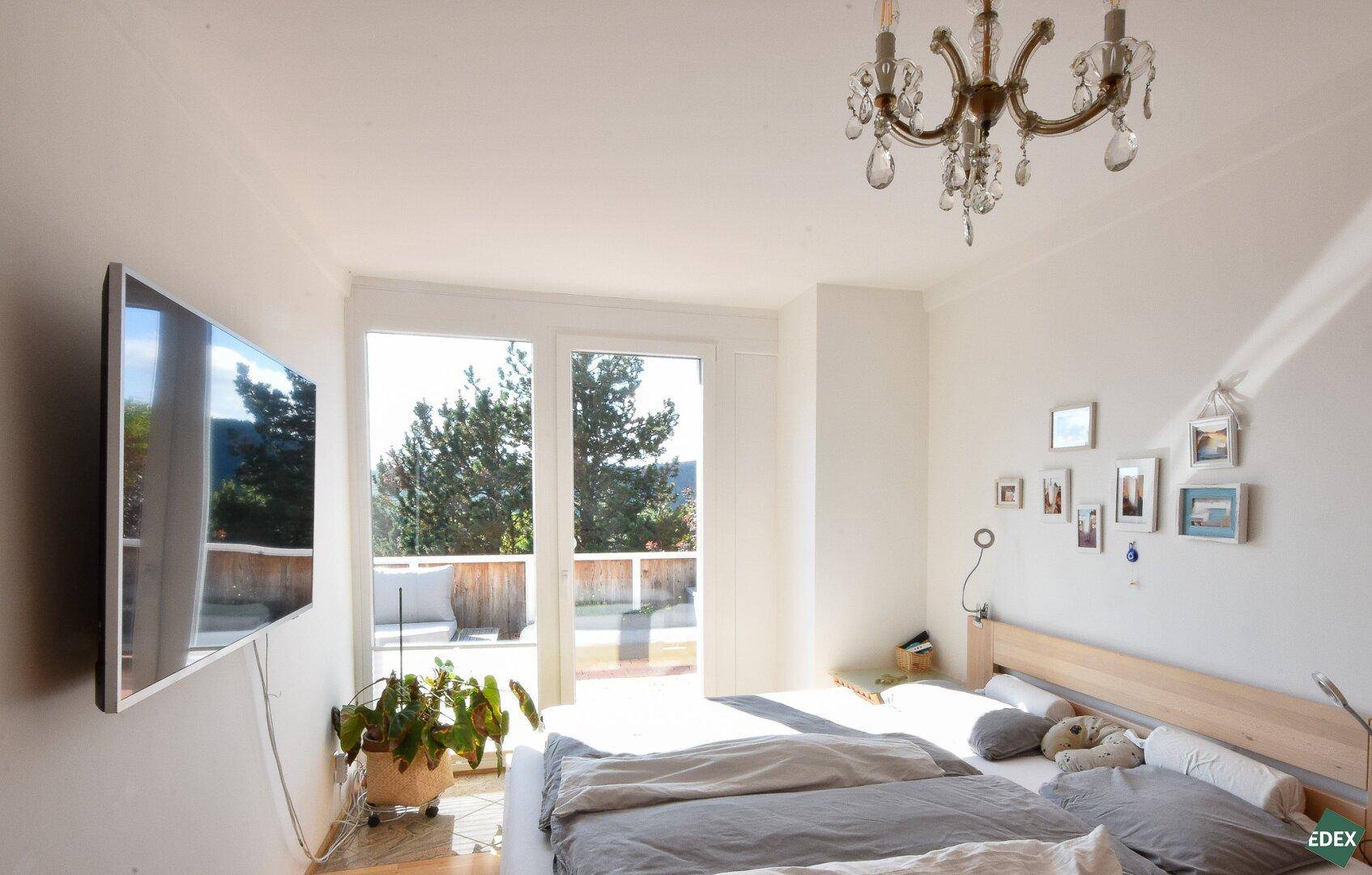 Helles Schlafzimmer mit Doppelbett, Holzboden und Zugang zu einem Balkon oder einer Terrasse.