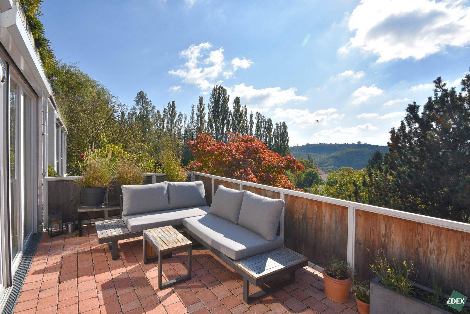 Sonniger Terrassenbereich mit Loungemöbeln und Panoramablick auf die umliegende Landschaft.