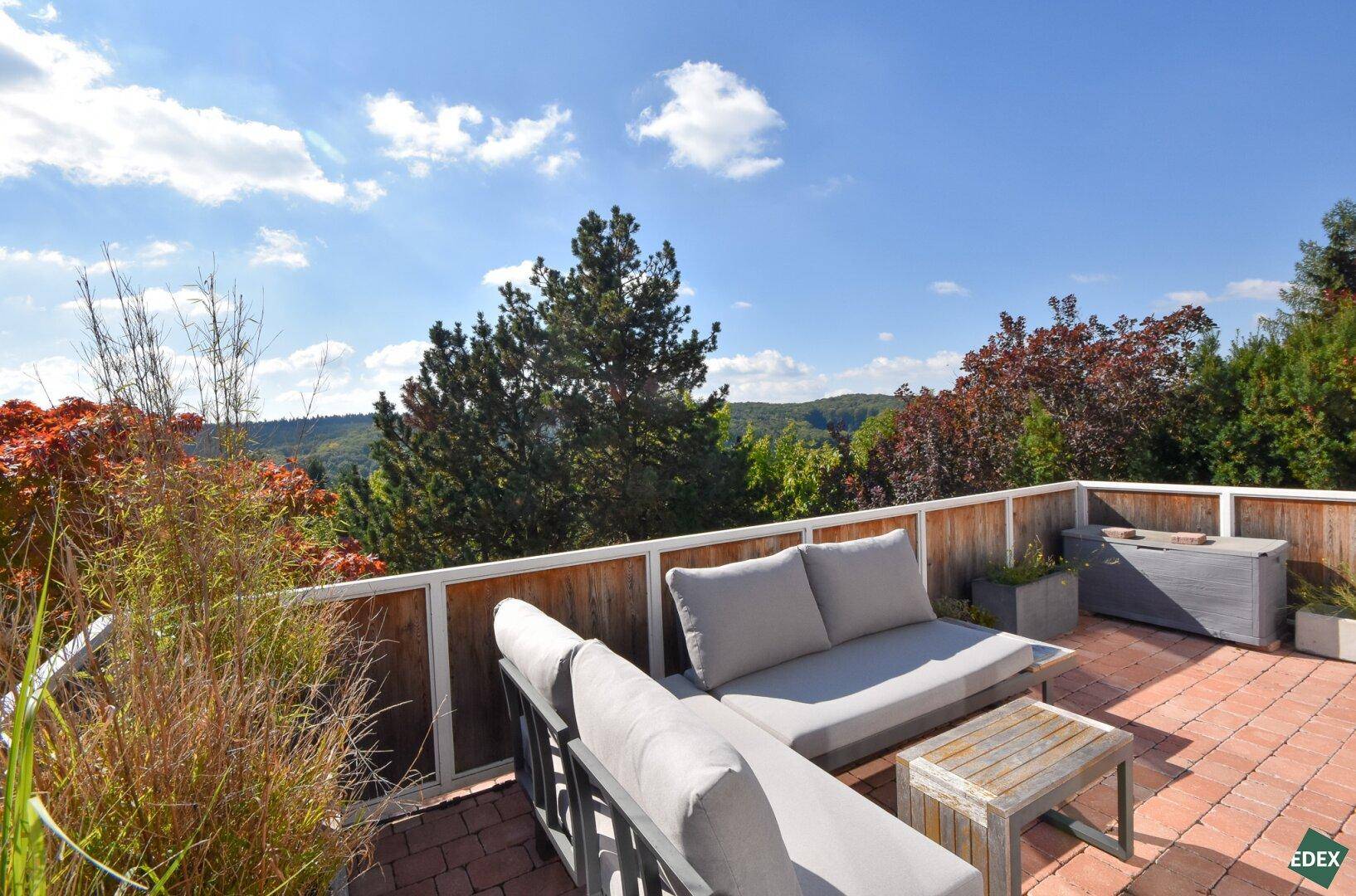 Geräumige Dachterrasse mit bequemen Loungemöbeln und weitem Blick ins Grüne unter blauem Himmel.