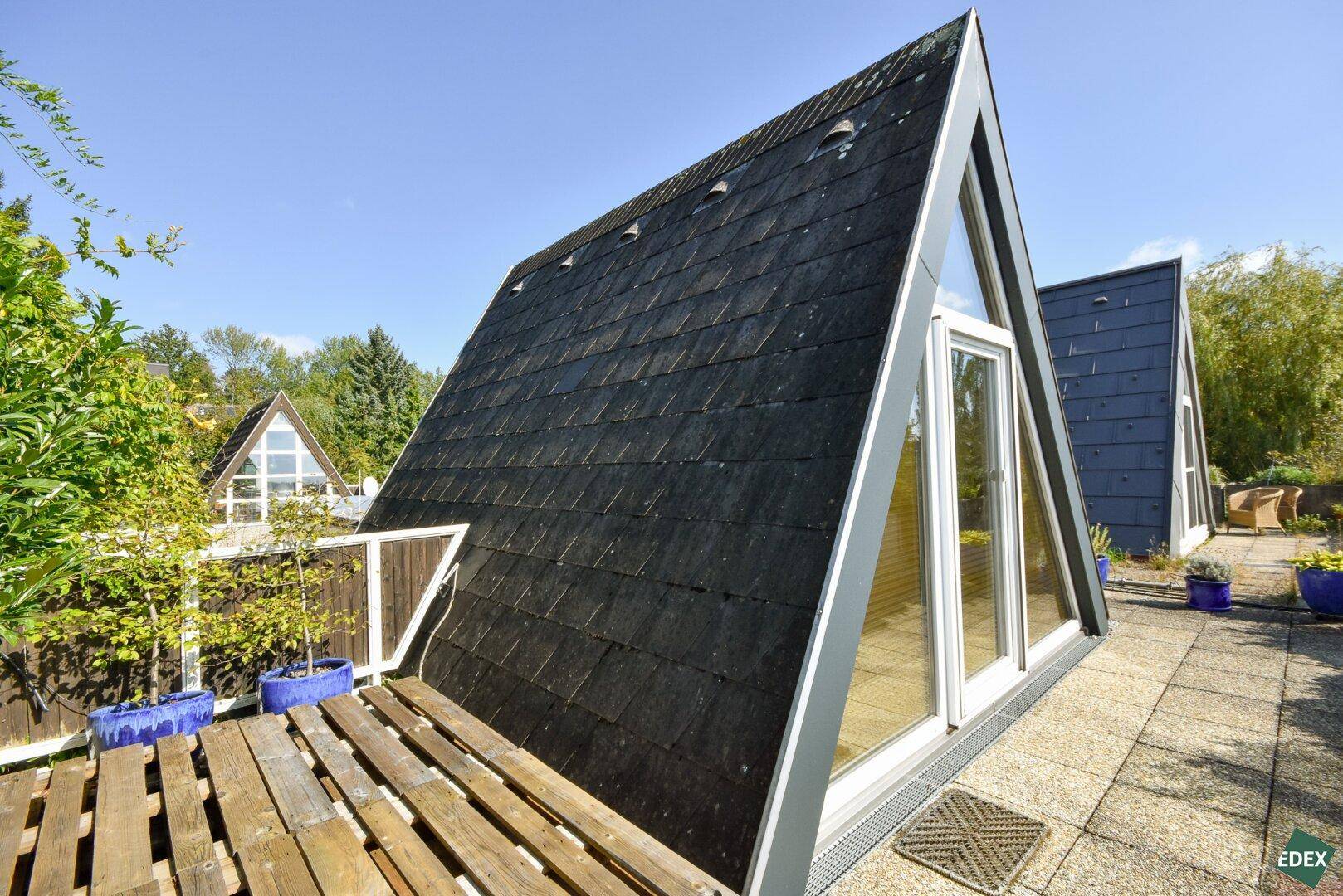 Außergewöhnliche Architektur mit spitzem Dach und Dachterrasse unter blauem Himmel.