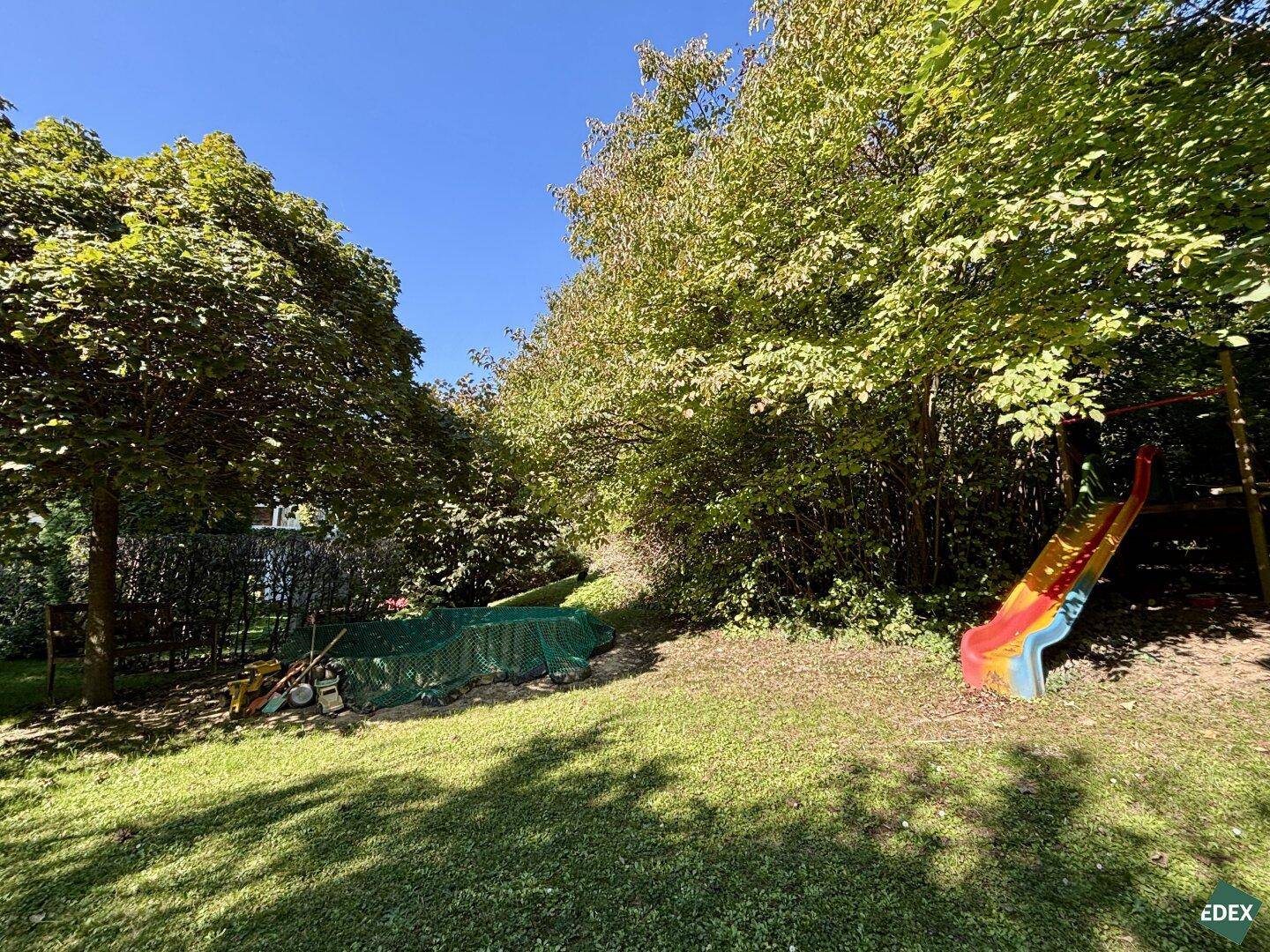 Natürlicher Gartenbereich mit einer bunten Rutsche und dichtem Baumbestand im Hintergrund.