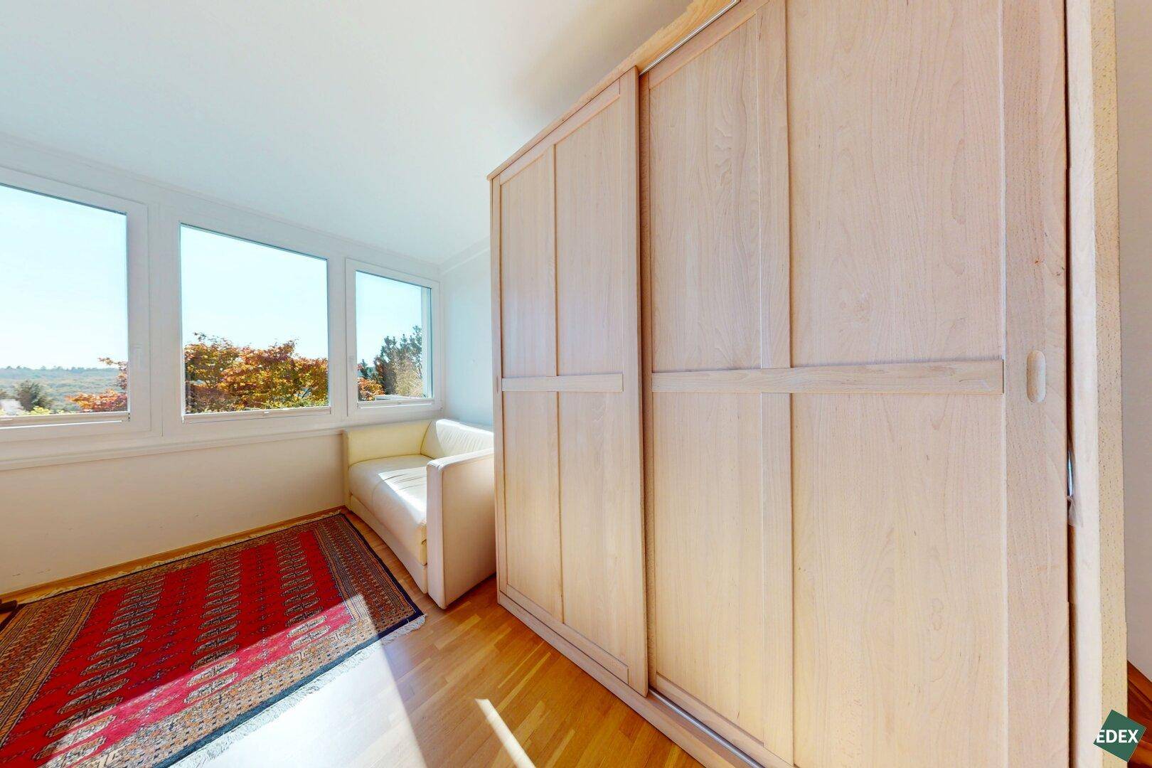 Helles Schlafzimmer mit Einbauschrank, Holzboden und Fenstern mit Weitblick ins Grüne.