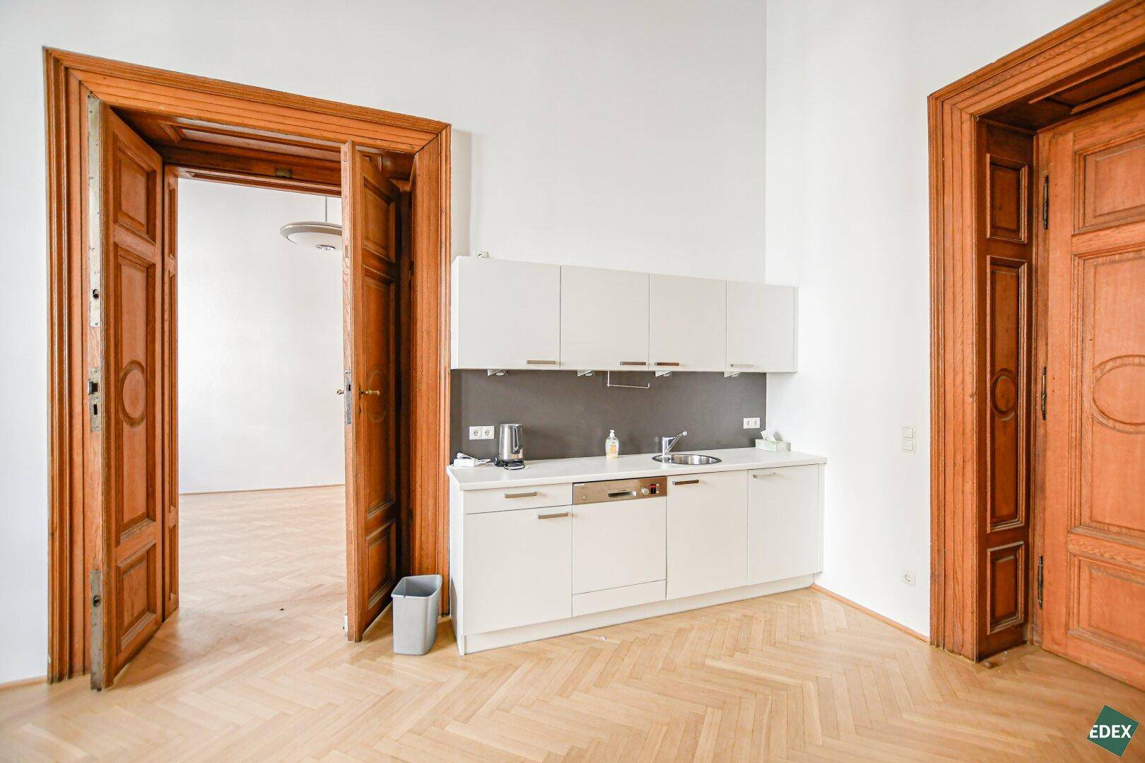Moderne, kompakte Küchenzeile mit weißen Schränken, Spülmaschine und Fischgrätparkettboden.