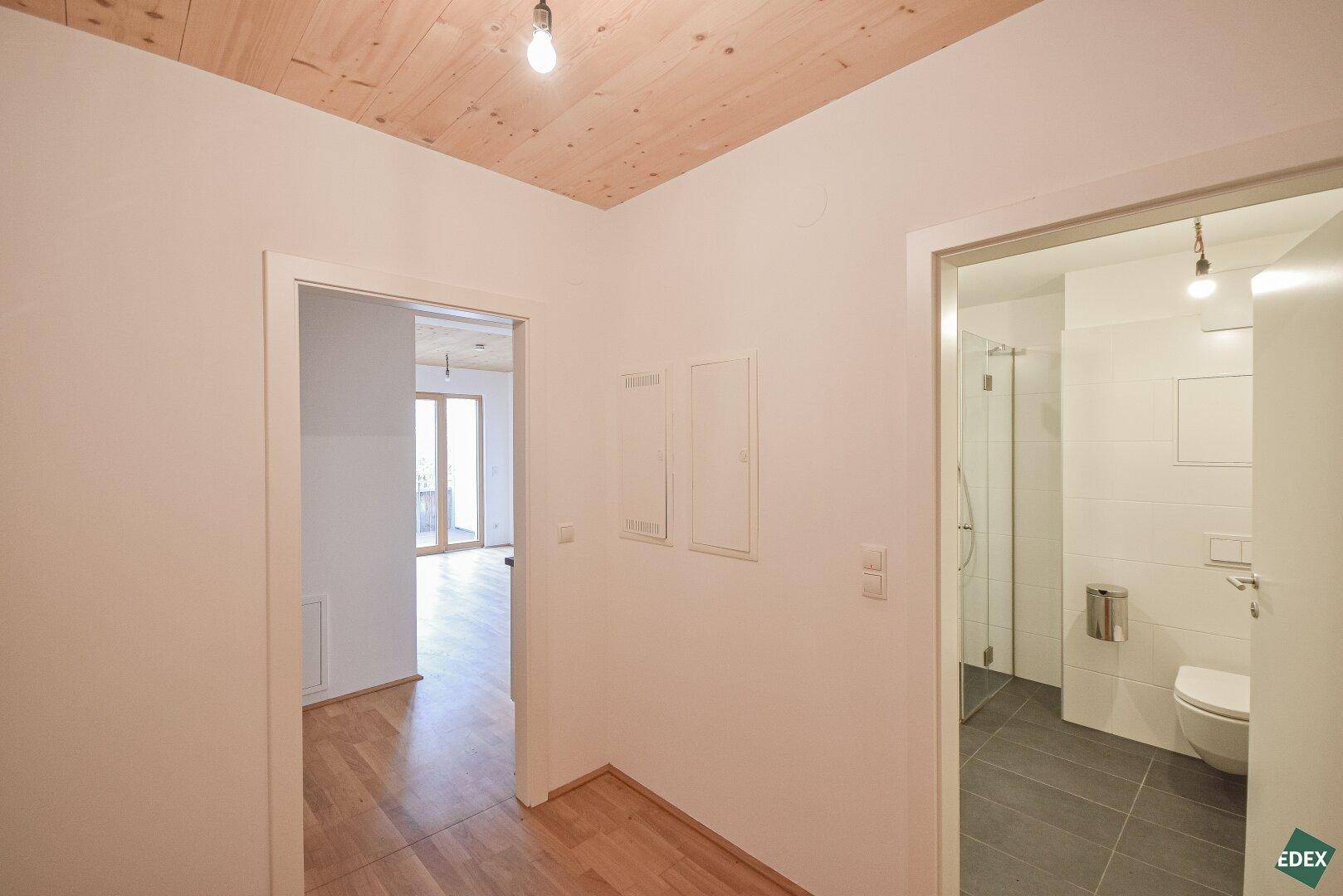 Heller Flur mit Holzboden und Zugang zu weiteren Zimmern, inklusive einem modernen Badezimmer.