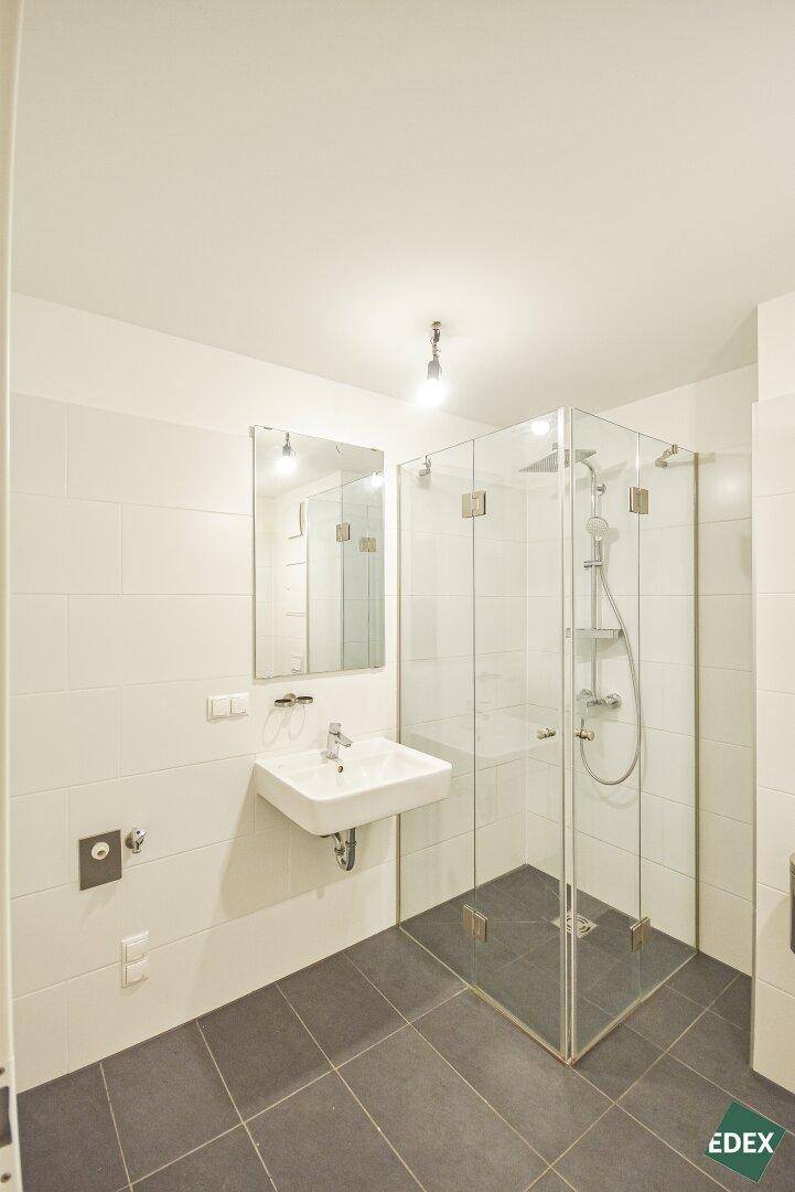 Modernes Badezimmer mit weißen Fliesen, dunklem Fliesenboden, Waschbecken und Glasduschkabine.
