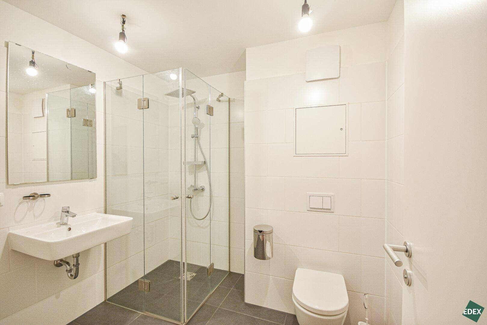 Helles Badezimmer mit Dusche, WC, Waschbecken und modernen Fliesen in Weiß und Grau.