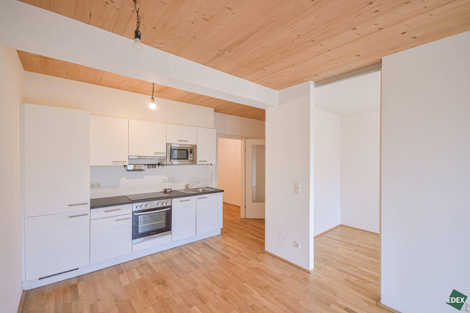 Moderne Einbauküche mit weißen Schränken, integrierten Geräten und Holzboden in offenem Bereich.