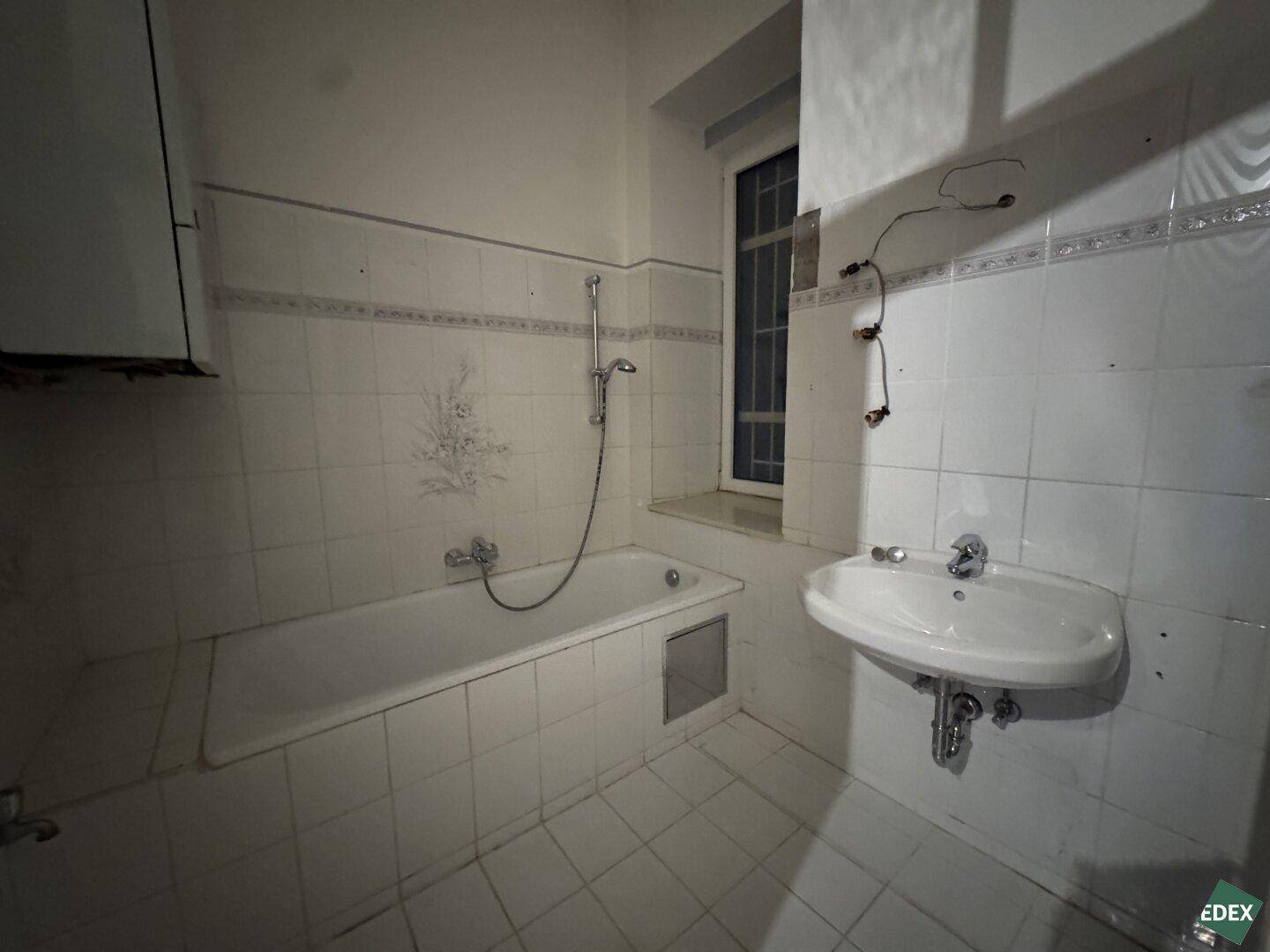 Badezimmer mit Badewanne, Waschbecken und Fliesen, benötigt eine Modernisierung.