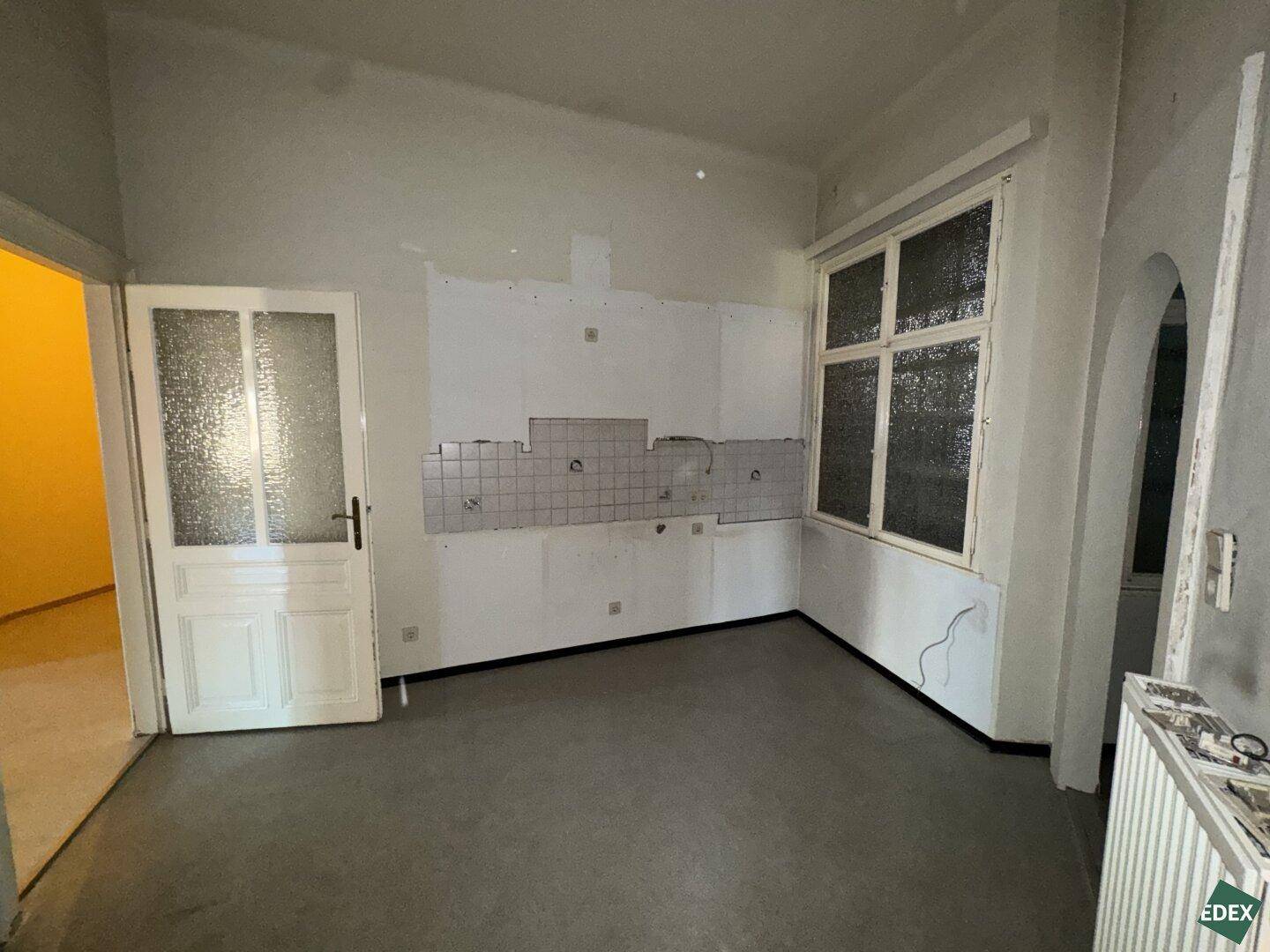Leere Küche mit Fliesenresten und großem Fenster, bereit für eine neue Einbauküche.