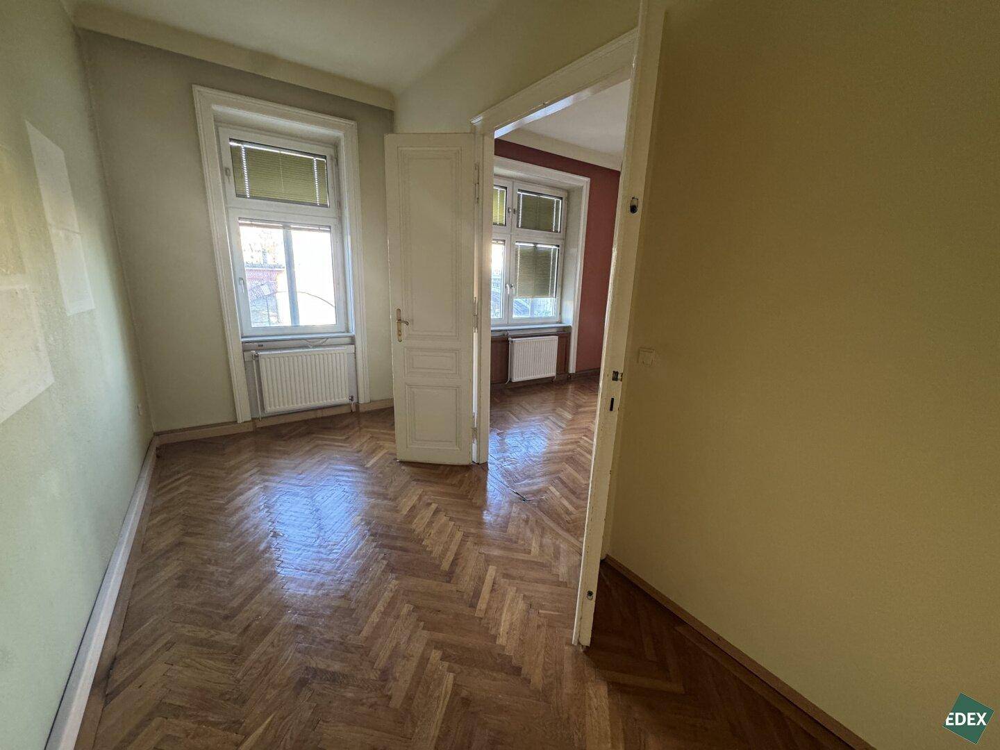 Gemütliches Zimmer mit Fischgrätparkett und zwei Fenstern, bietet Potenzial für individuelle Gestaltung.