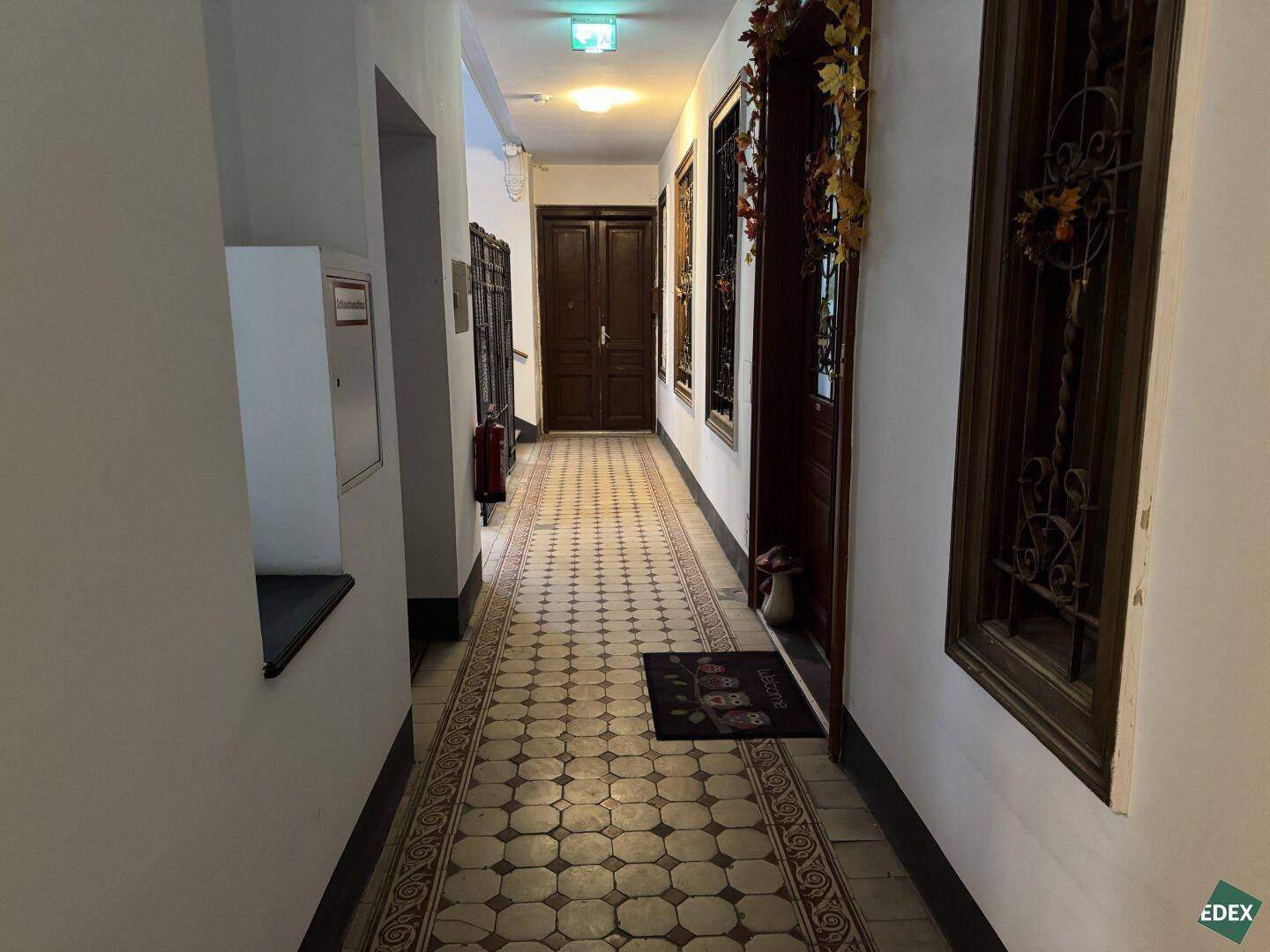Langer Flur in einem Altbau mit gemustertem Fliesenboden und Holztüren, charmantes Ambiente.