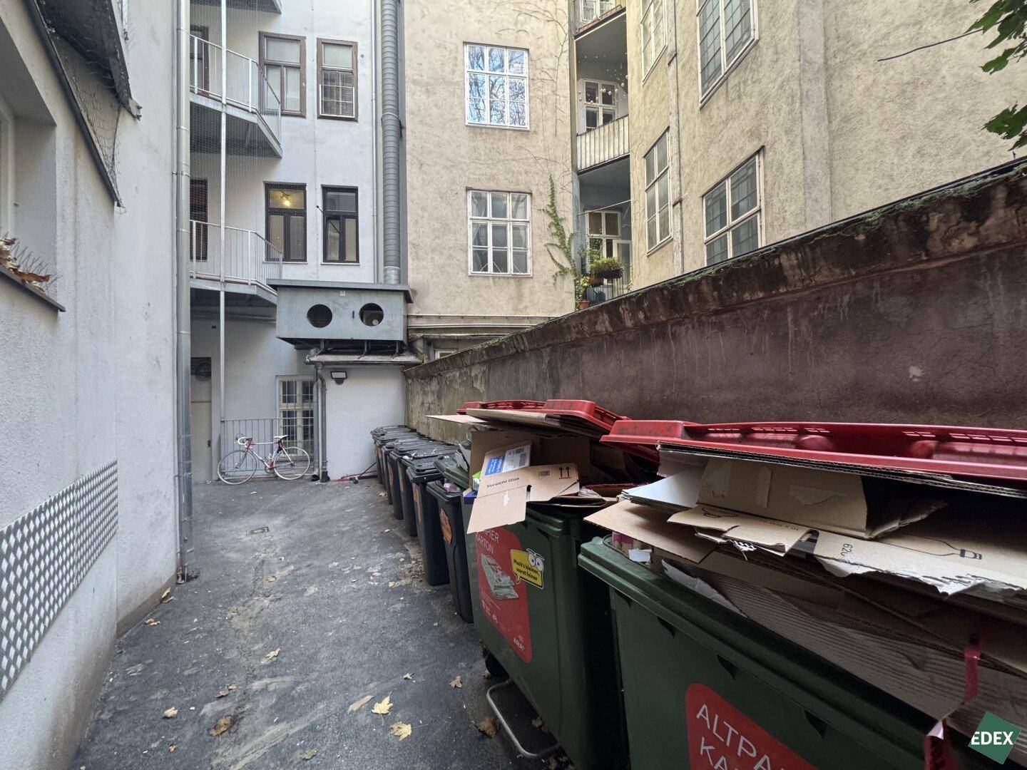 Hinterhof mit Mülltonnen und Fahrradabstellplatz zwischen den Gebäuden, funktionaler Außenbereich.