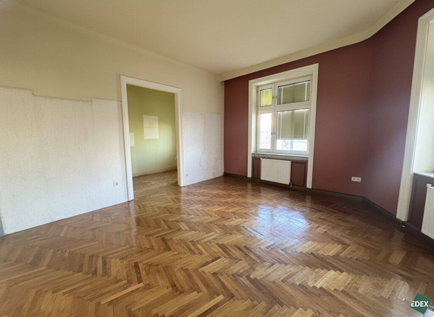 Helles Zimmer mit klassischem Fischgrätparkett und farbigen Wänden, ideal für eine Renovierung.