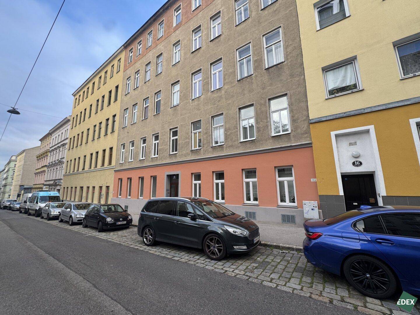 Straßenansicht eines Mehrfamilienhauses mit parkenden Autos und klassischer Altbaufassade.