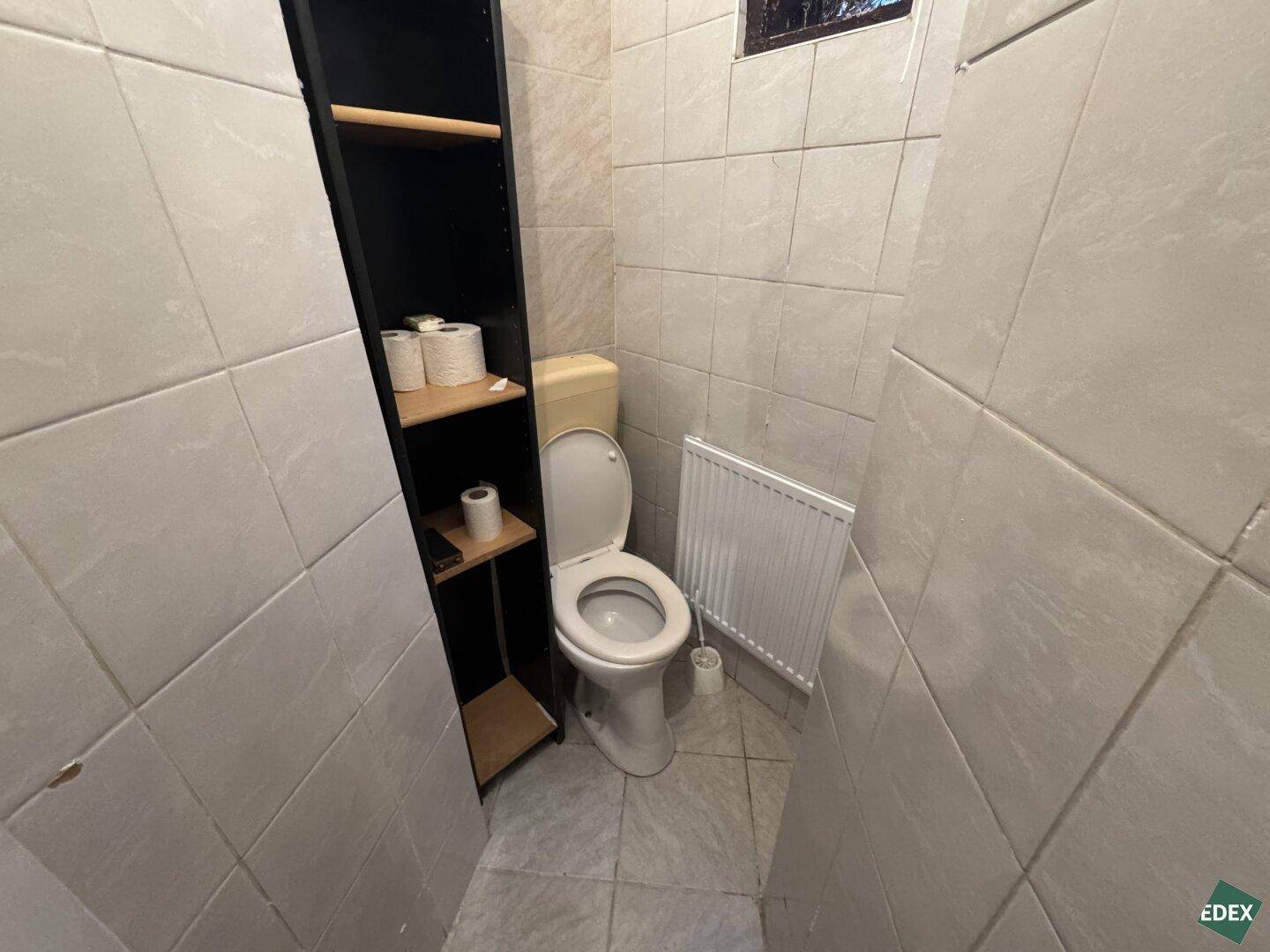 Separate Toilette mit WC, Heizkörper und Fliesen an Wänden und Boden für einfache Pflege.