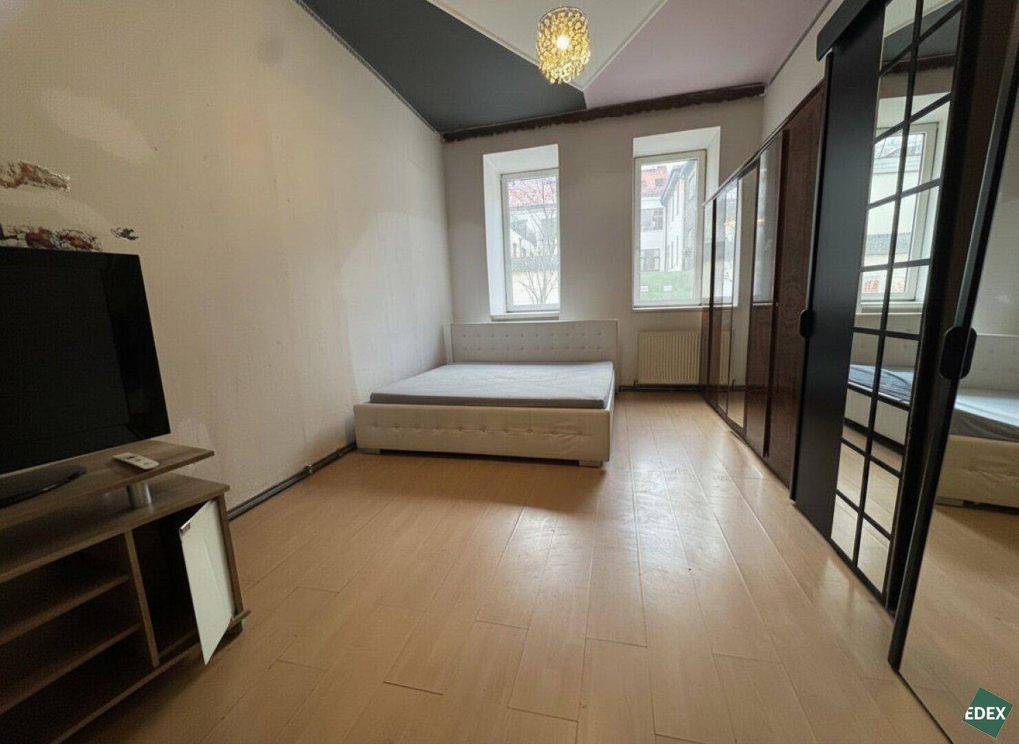 Schlafzimmer mit Doppelbett, Holzfußboden und Spiegelschränken, hell durch große Fenster.