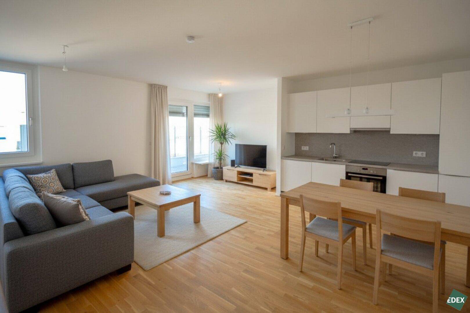 Offener Wohn-Essbereich mit integrierter Küche, Holzboden und Zugang zum Balkon.