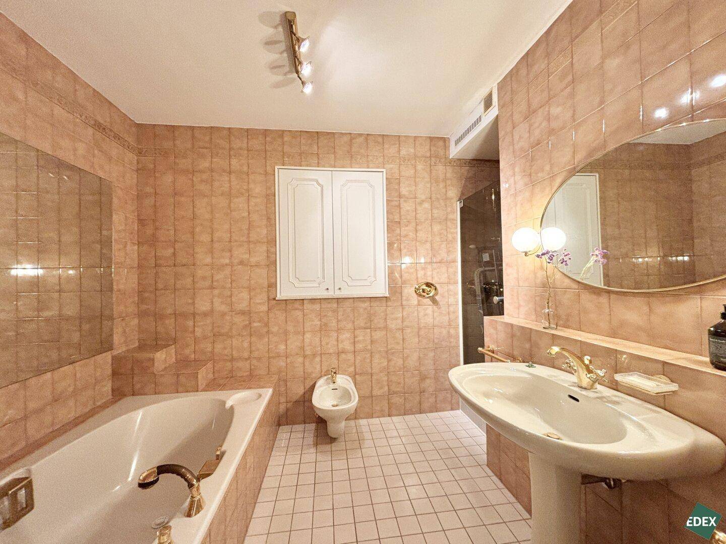 Badezimmer im 80er-Jahre-Stil mit pfirsichfarbenen Fliesen, Badewanne, Bidet und Waschtisch.