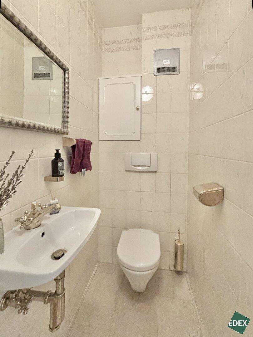 Helles Gäste-WC mit wandhängender Toilette, kleinem Waschbecken und beigefarbenen Fliesen.