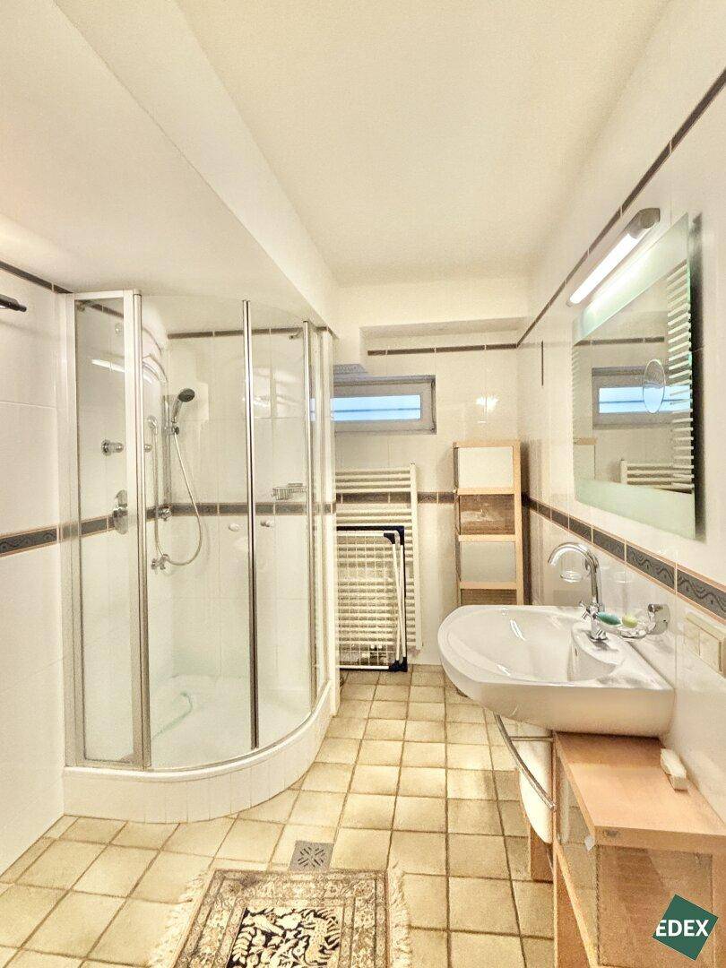 Badezimmer mit Duschkabine, Waschbecken, beheiztem Handtuchhalter und Fliesenboden.