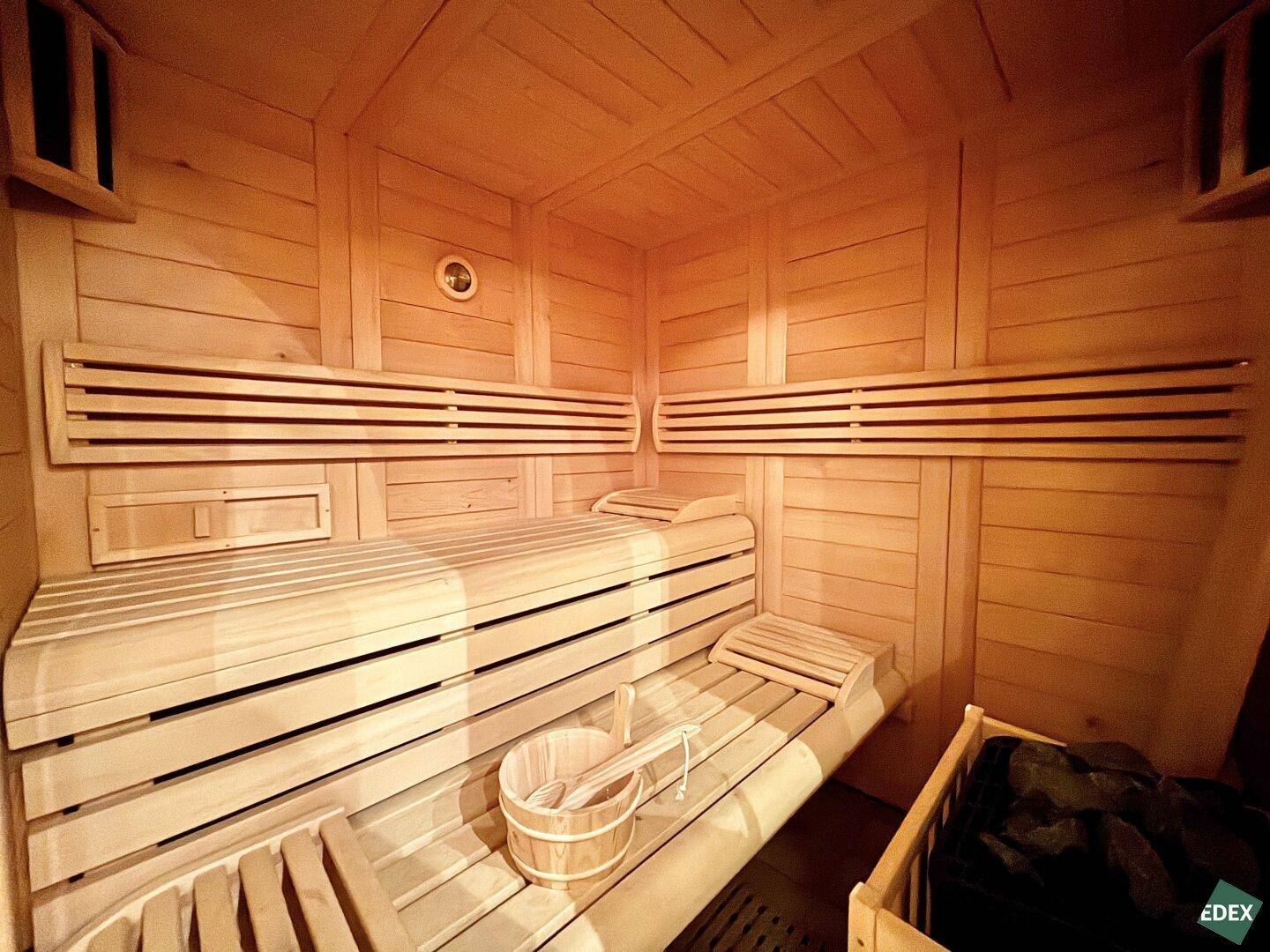 Holzvertäfelte Sauna mit mehreren Bänken und traditionellem Saunaeimer.