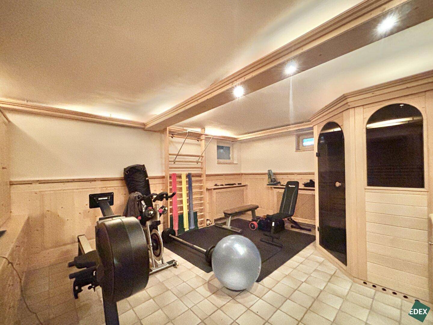 Fitnessraum im Untergeschoss mit verschiedenen Geräten und integrierter Sauna.