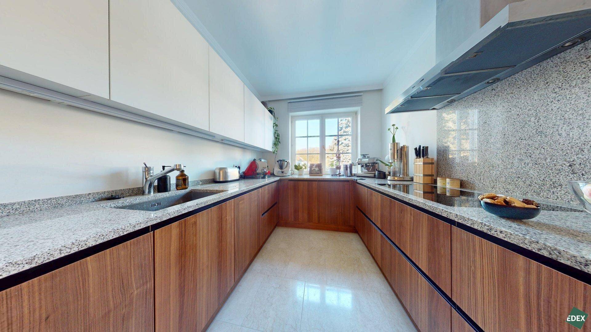 Moderne Küche mit Holzfronten, weißen Oberschränken und Arbeitsplatten aus hellem Granit.