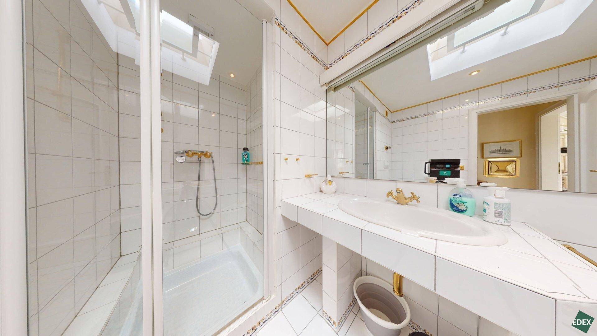 Badezimmer mit Duschkabine, Waschbecken, großem Spiegel und Dachfenster für Tageslicht.