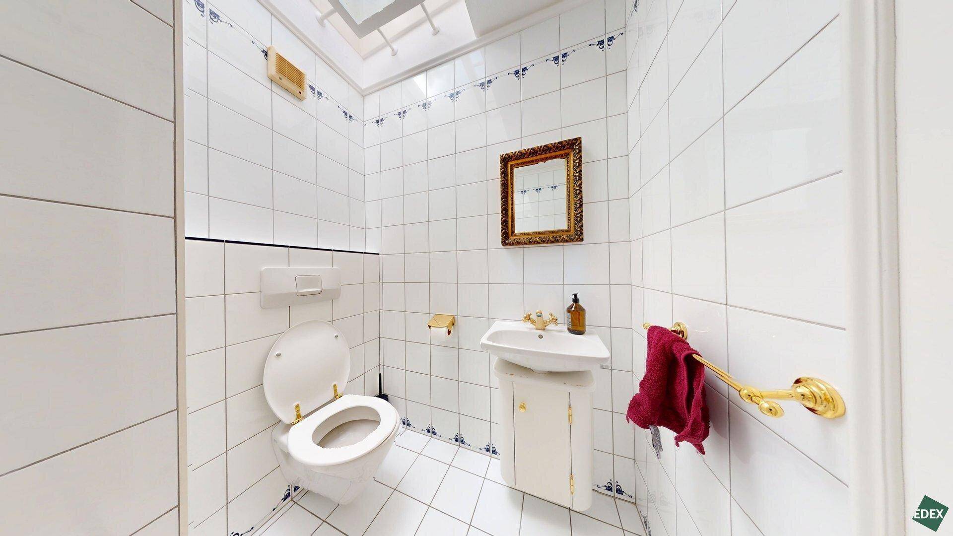 Kleines Gäste-WC mit Toilette, Waschbecken und weißen Fliesen mit blauen Details im 80er-Jahre-Stil.