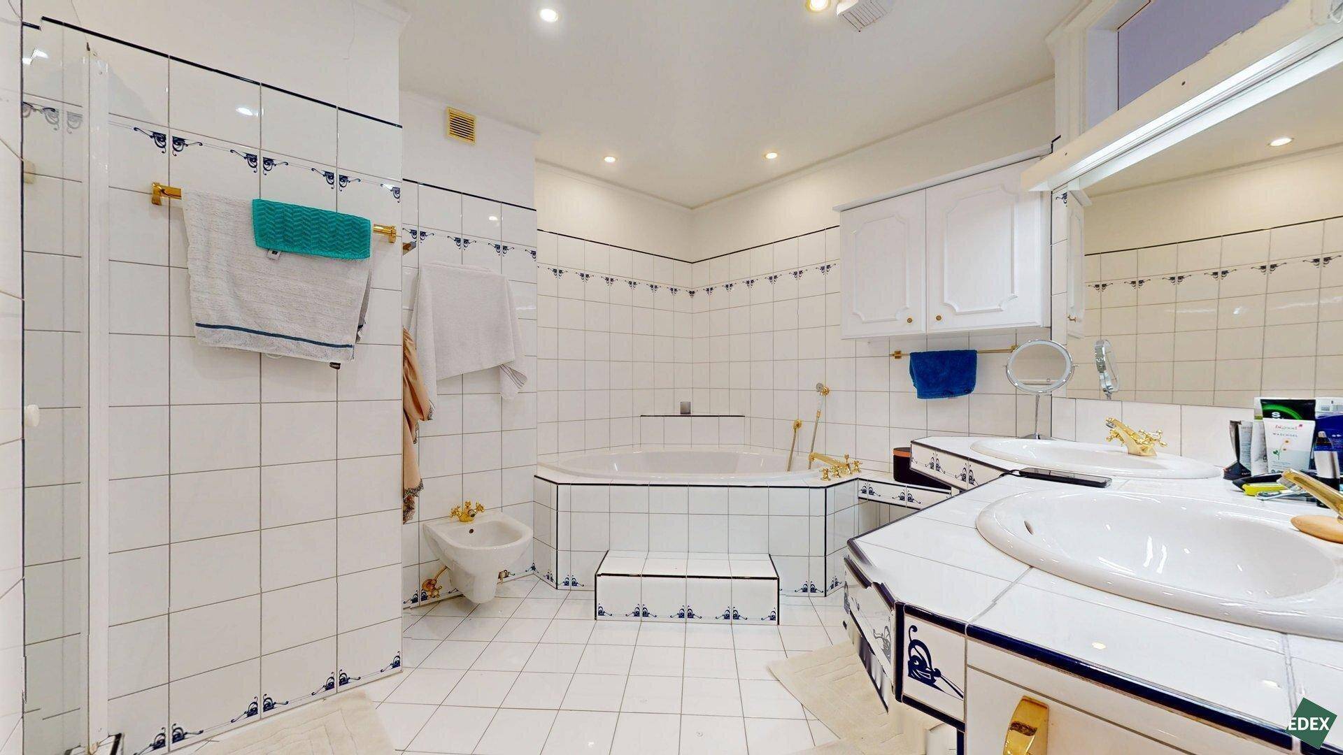 Geräumiges Badezimmer mit Doppelwaschbecken, Badewanne, Bidet und blauen Akzentfliesen im 80er-Jahre-Stil.