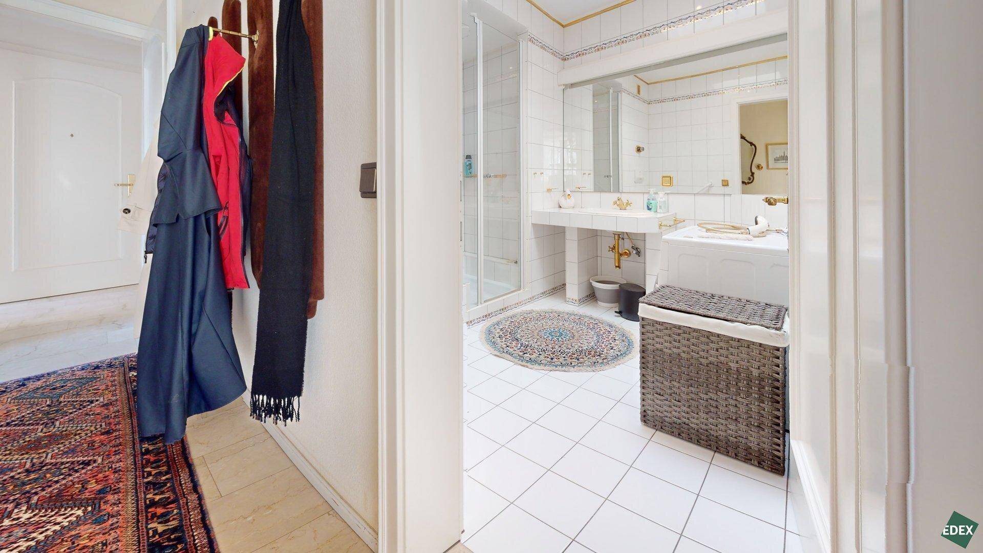 Flur mit Garderobe und Blick in ein hell gefliestes Badezimmer mit Duschkabine.