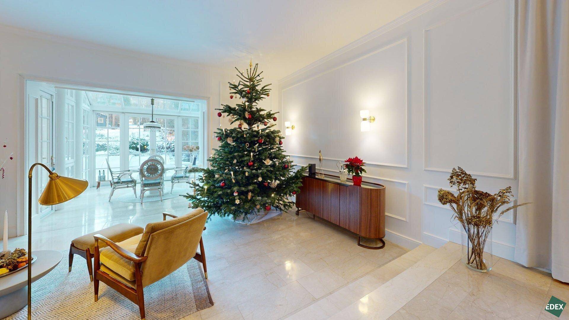 Festlich geschmücktes Wohnzimmer mit Weihnachtsbaum, elegantem Sideboard und Zugang zum Wintergarten.