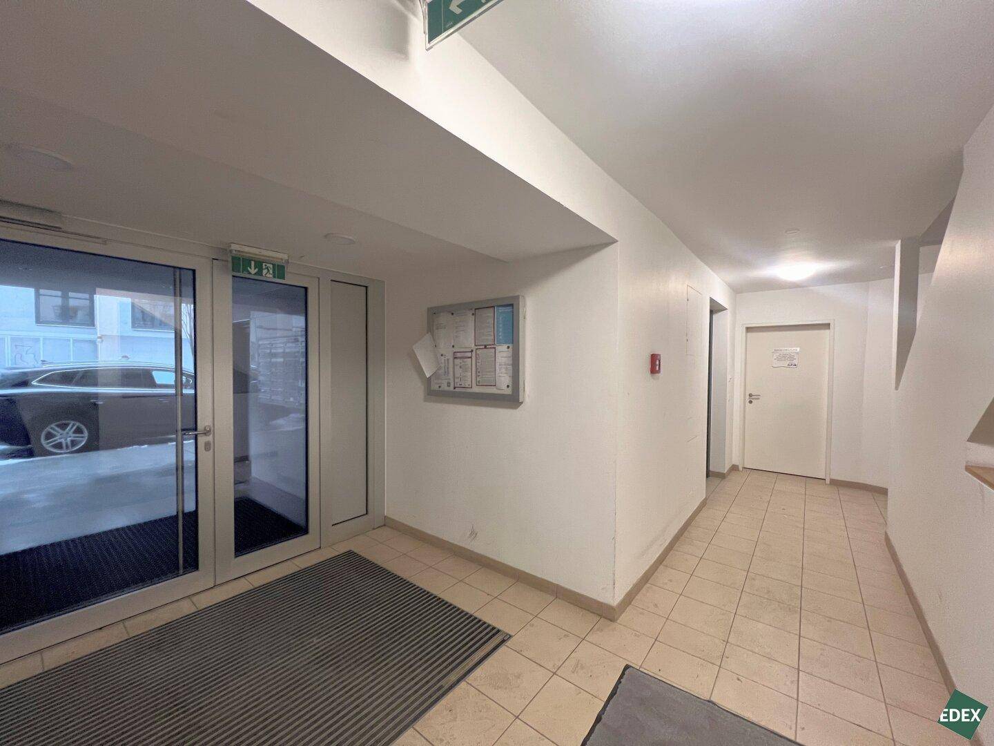 Eingangsbereich des Gebäudes mit großen Glastüren und Fliesenboden.