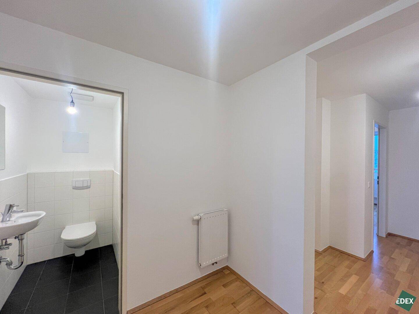 Flur mit Zugang zu einem Gäste-WC, ausgestattet mit Heizkörper und Holzboden.